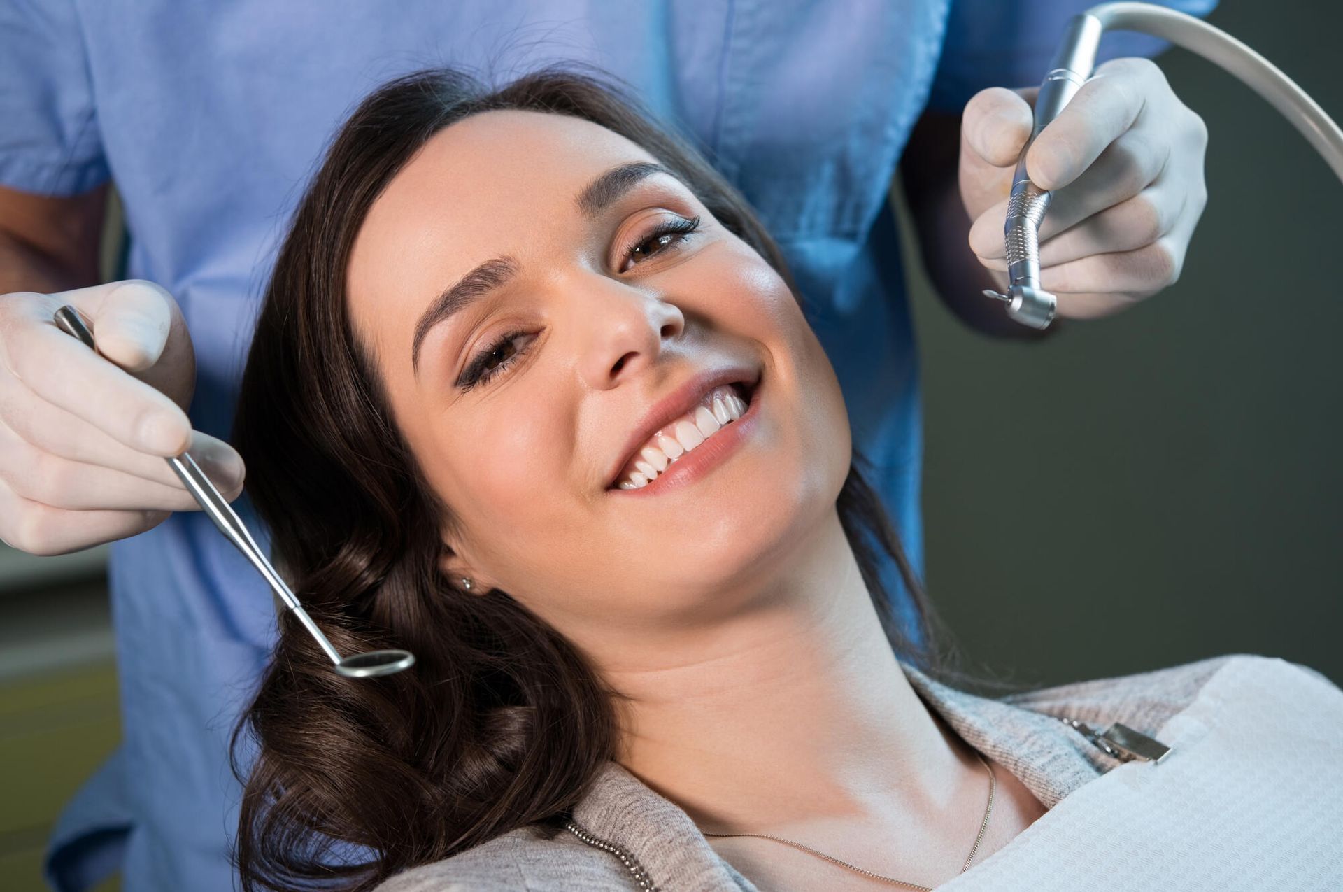 Smiling patient in a dental chair as a dentist holds tools nearby