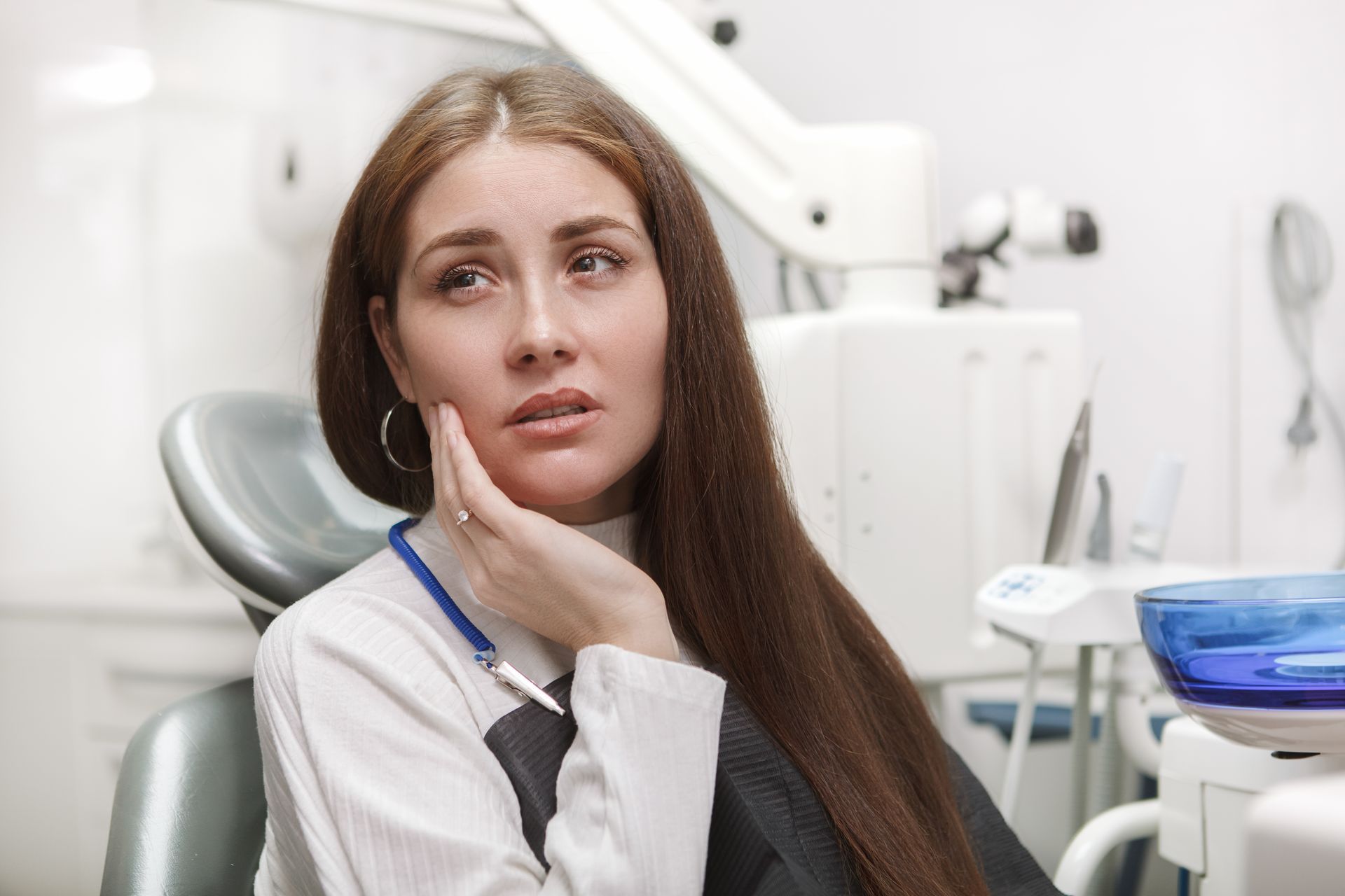 Woman in dental chair, holding cheek with pained expression, likely experiencing toothache.