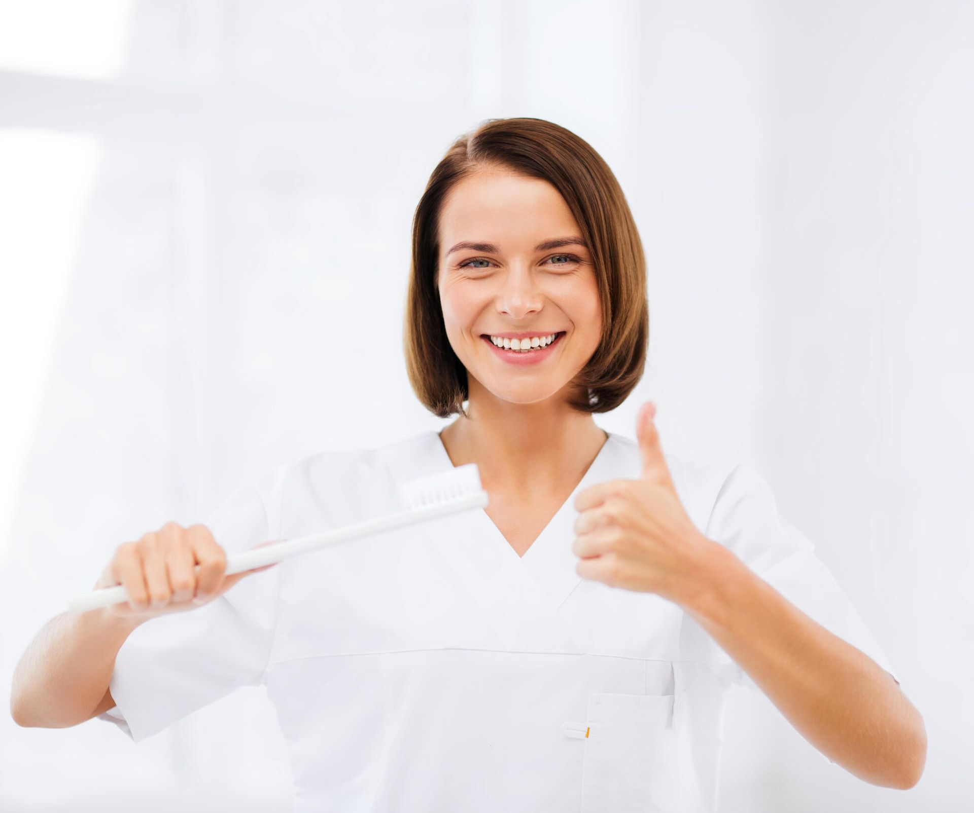 Smiling nurse in white scrubs holding a syringe and giving a thumbs-up