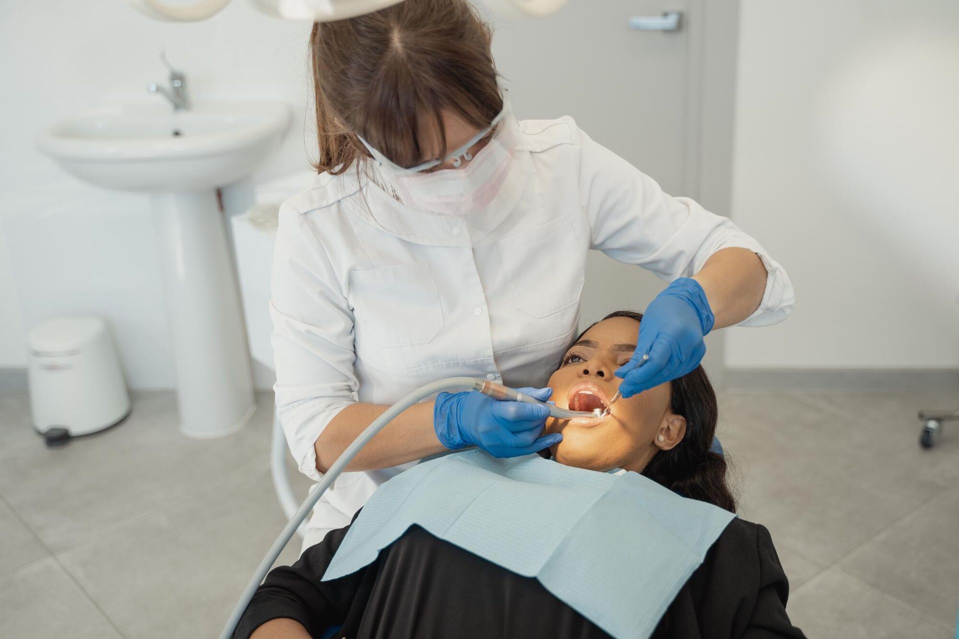 Dentist treating a patient in a clinic, with blue gloves and a bright exam light.