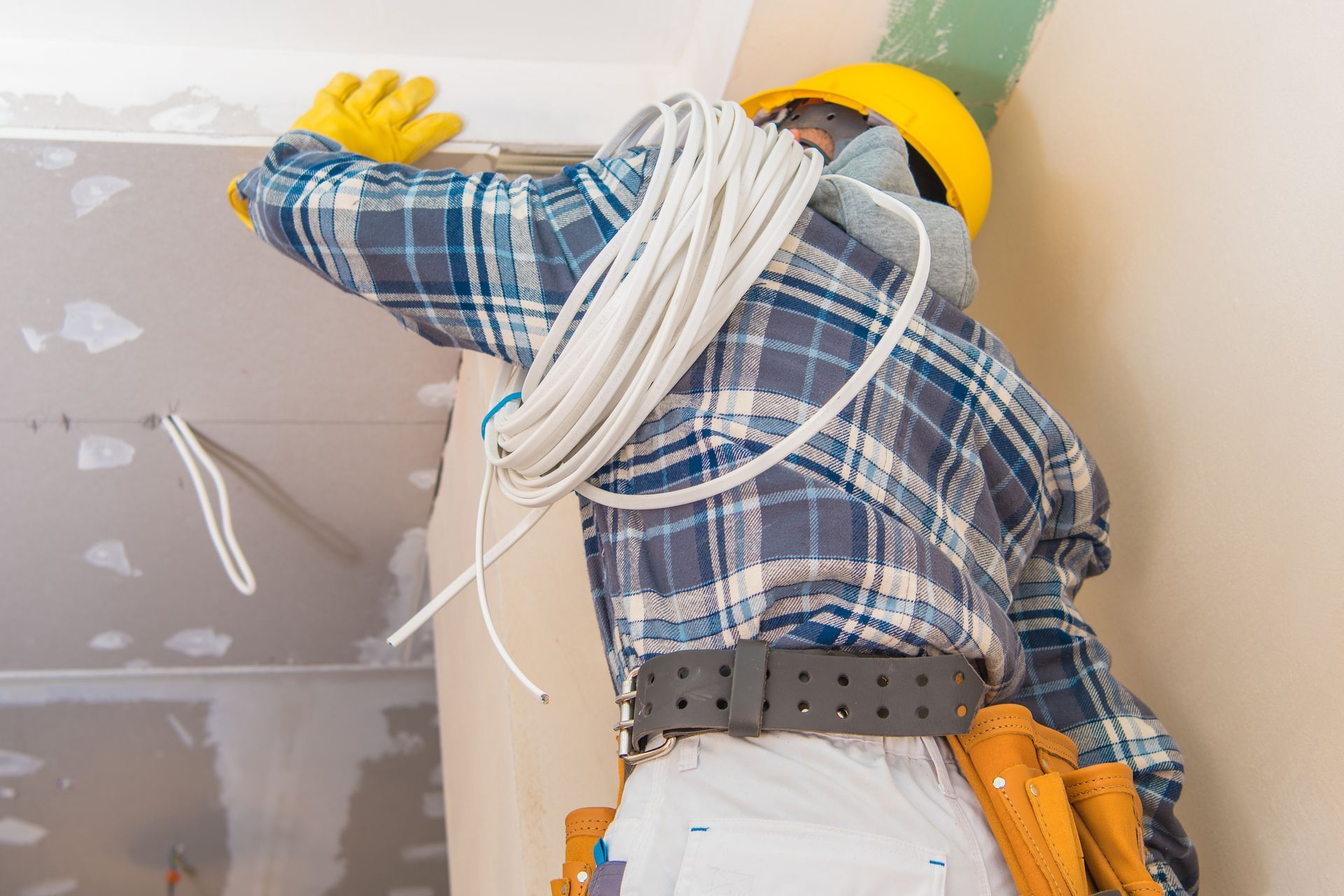 A commercial electrician is installing ceiling wiring. A commercial electrician is installing ceiling wiring.