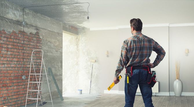 Worker holding a tool in a room with exposed brick, likely preparing for renovation and wall work