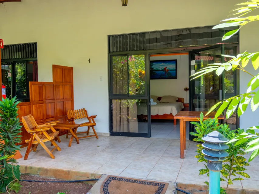 Patio abierto con sillas de mimbre, mesa de madera y puertas de cristal con vistas a un jardín.