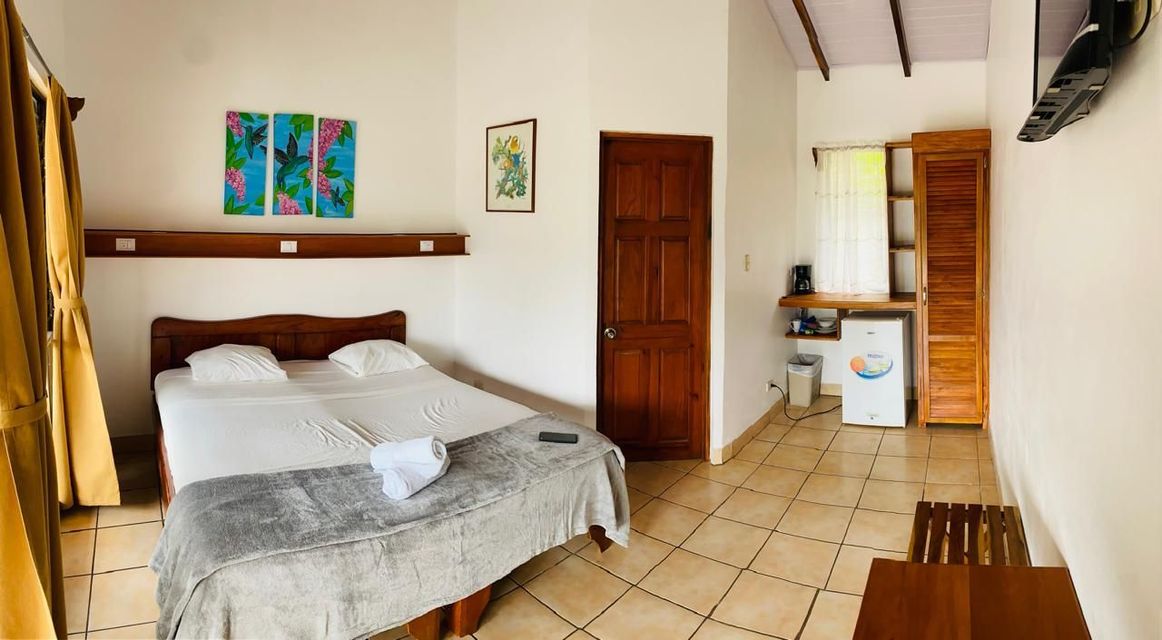 Habitación pequeña con cama, suelo de baldosas, puertas de madera y una cocina pequeña en la parte trasera.