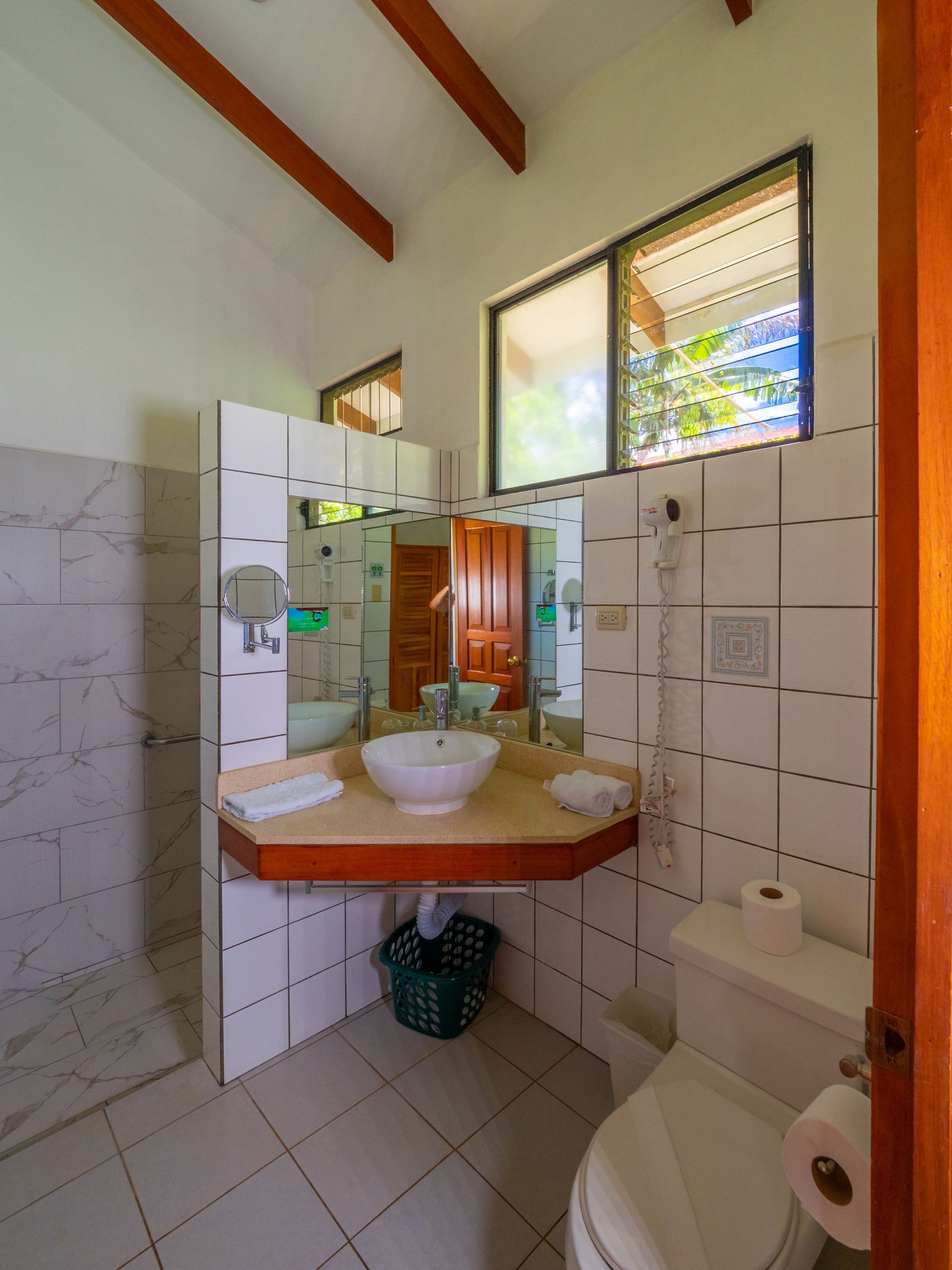 Baño pequeño con paredes alicatadas, lavabo de esquina, espejo, inodoro y ventanas que dejan entrar la luz natural.