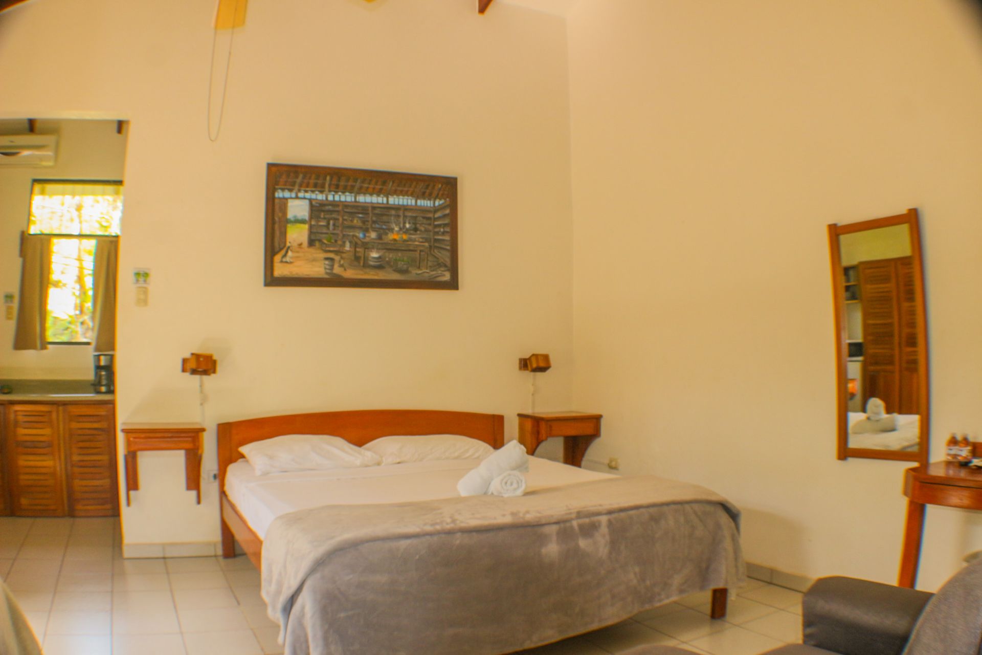 Habitación de hotel sencilla con cama, mesita, espejo y paredes de color beige cálido.