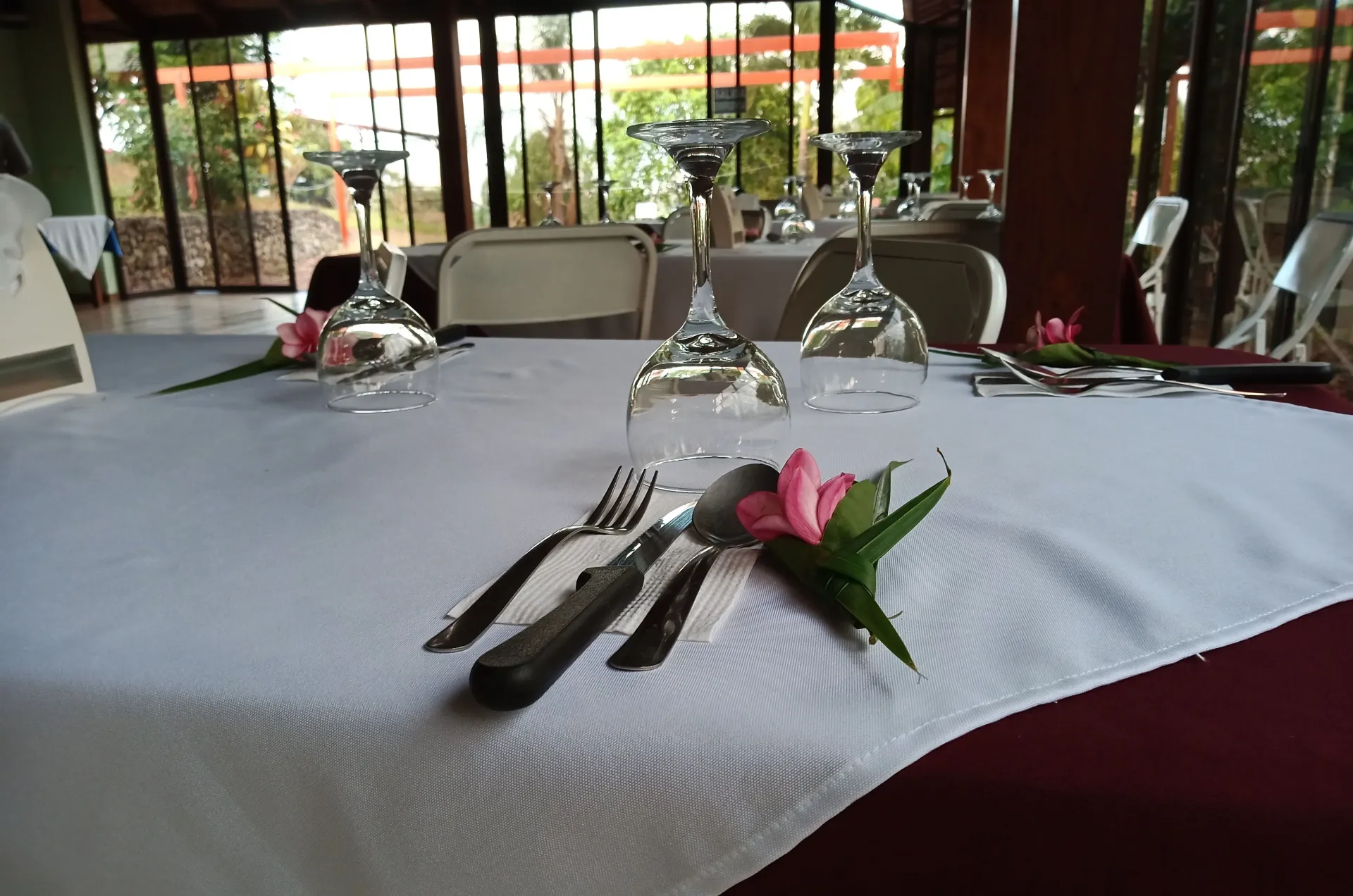 Dining table set with silverware, wine glasses, and a pink napkin in a bright restaurant