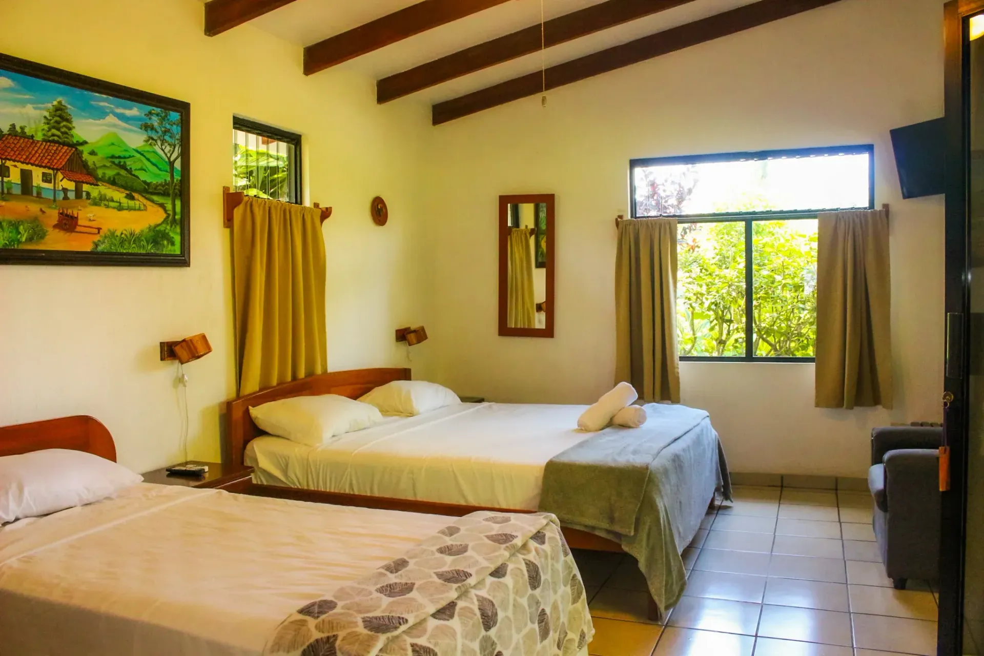 Habitación acogedora con dos camas, cortinas amarillas, suelo de baldosas y luz natural que entra por una ventana.