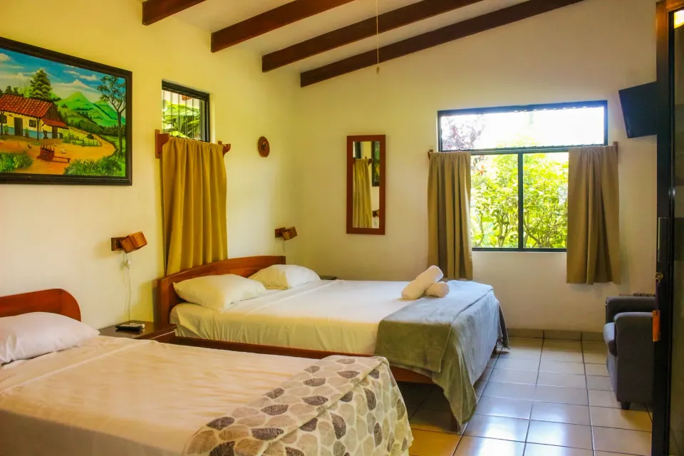 Habitación acogedora con dos camas, cortinas amarillas, suelo de baldosas y luz natural que entra por una ventana.