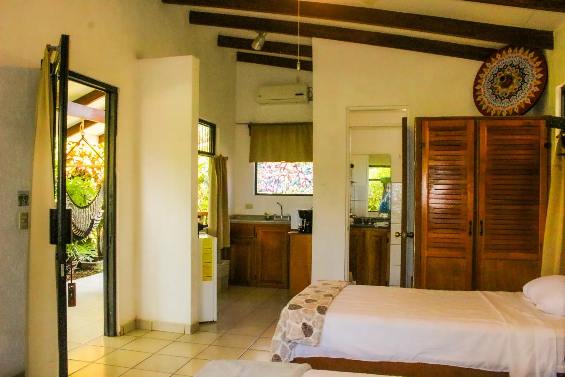 Habitación espaciosa con cama blanca, armario de madera, puertas abiertas y techo con vigas vistas.