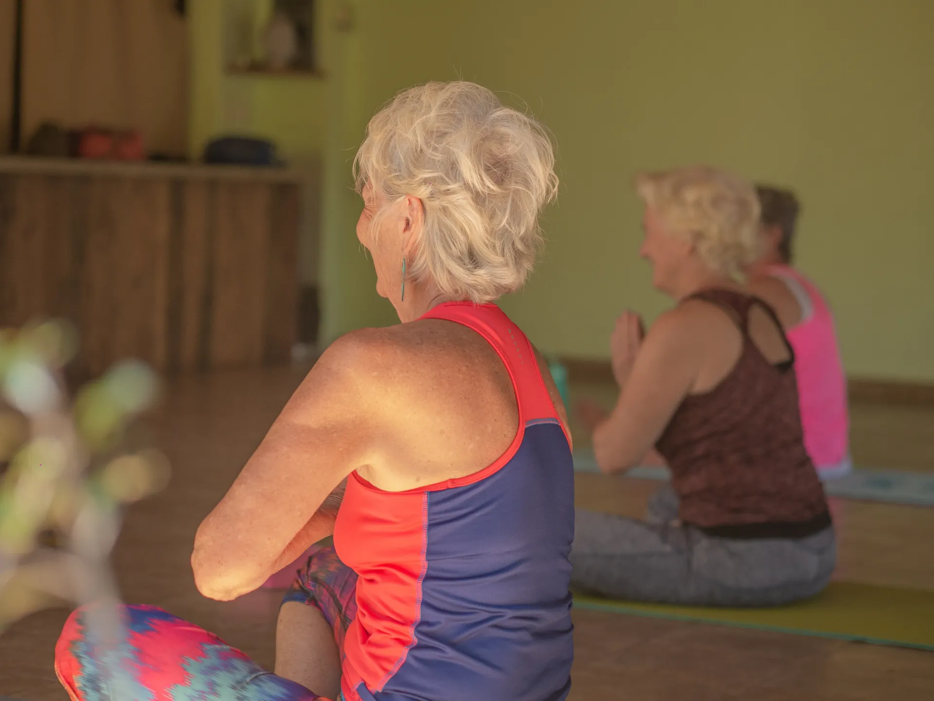 Two people seated on yoga mats in a studio, facing forward during a class.