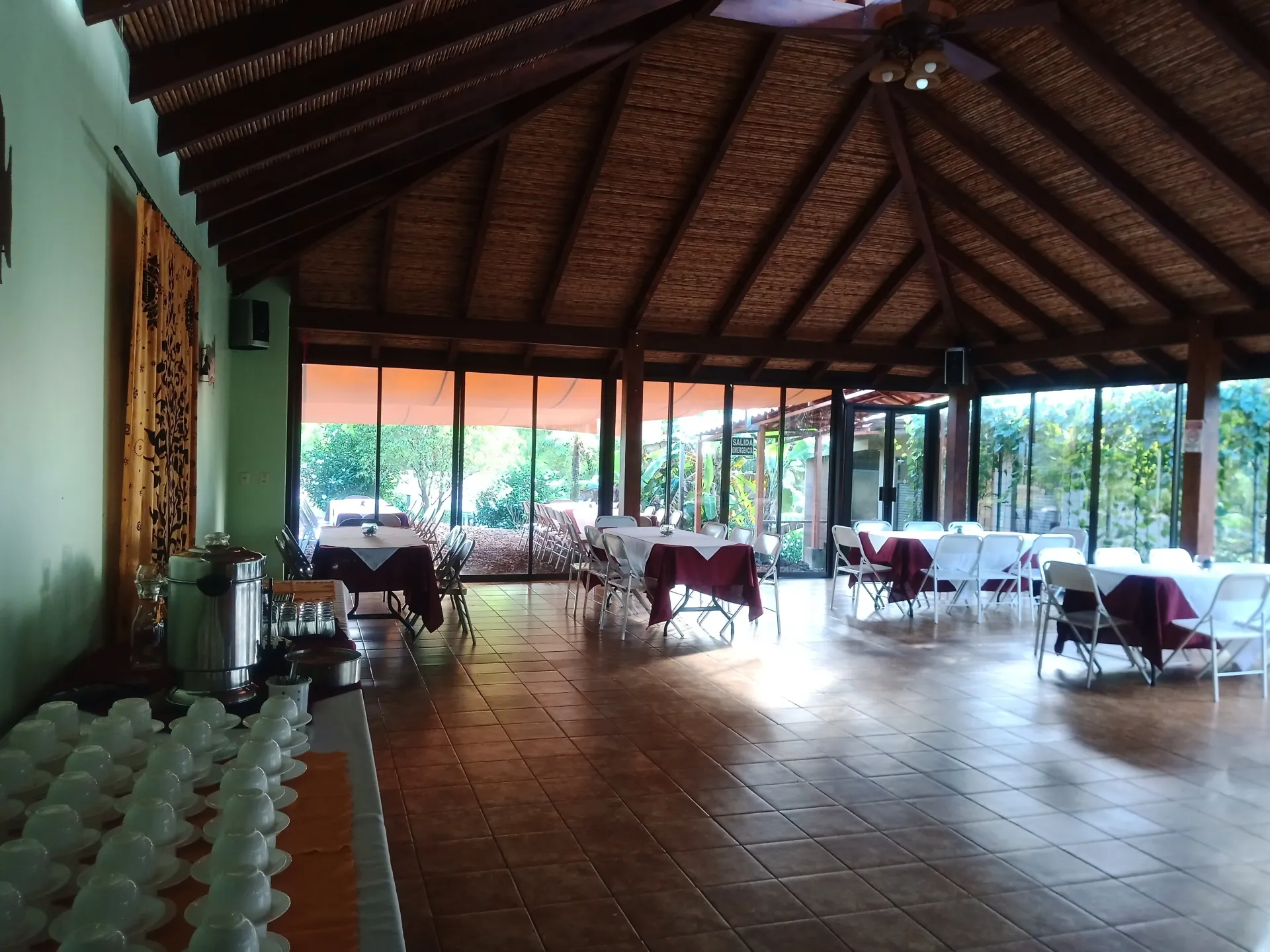 Open-air dining hall with thatched roof, wooden tables, and natural light from large windows