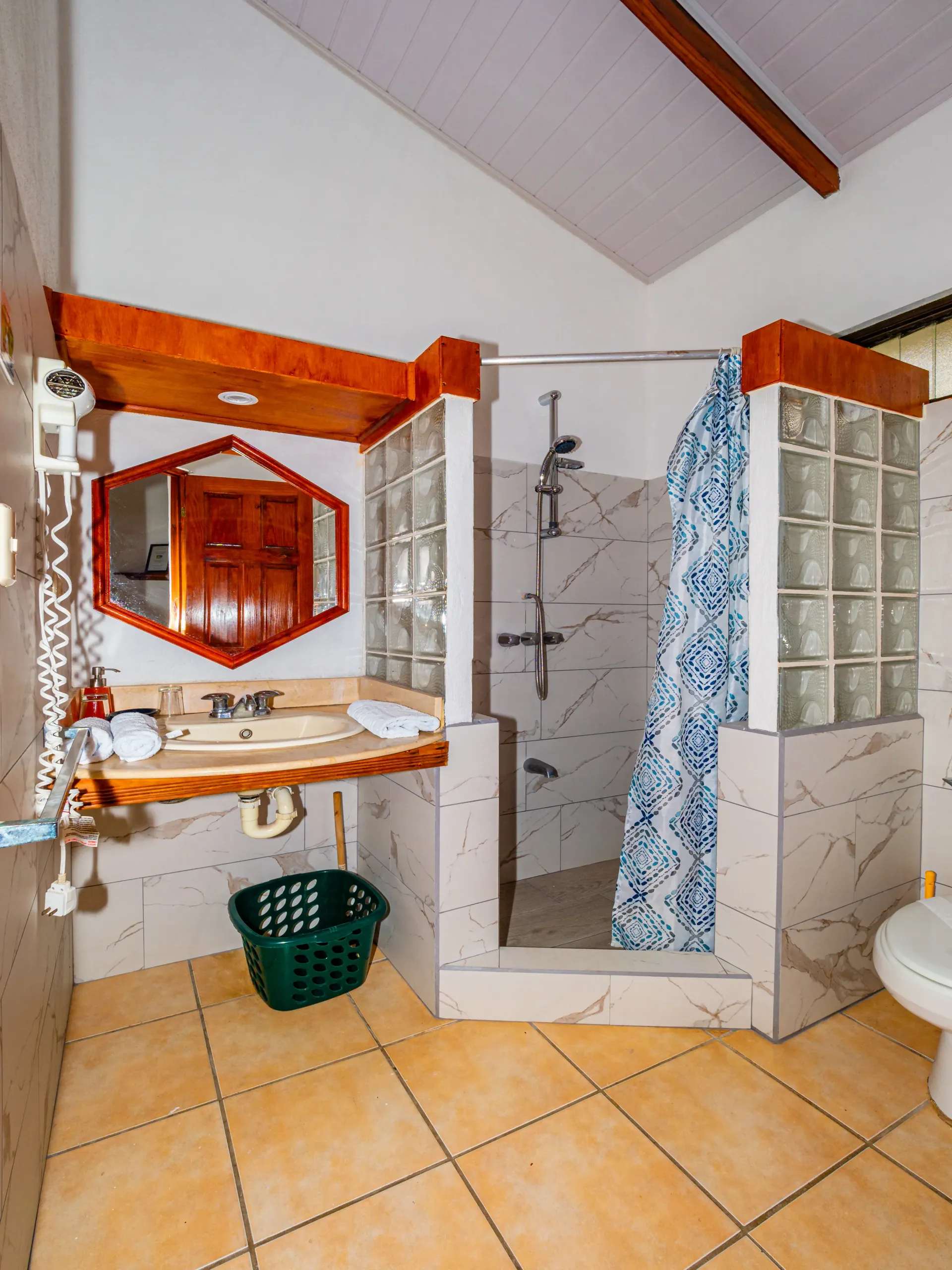 Baño con suelo de baldosas, espejo de pared, lavabo, ducha, mampara de bloques de vidrio y cortina de ducha azul.