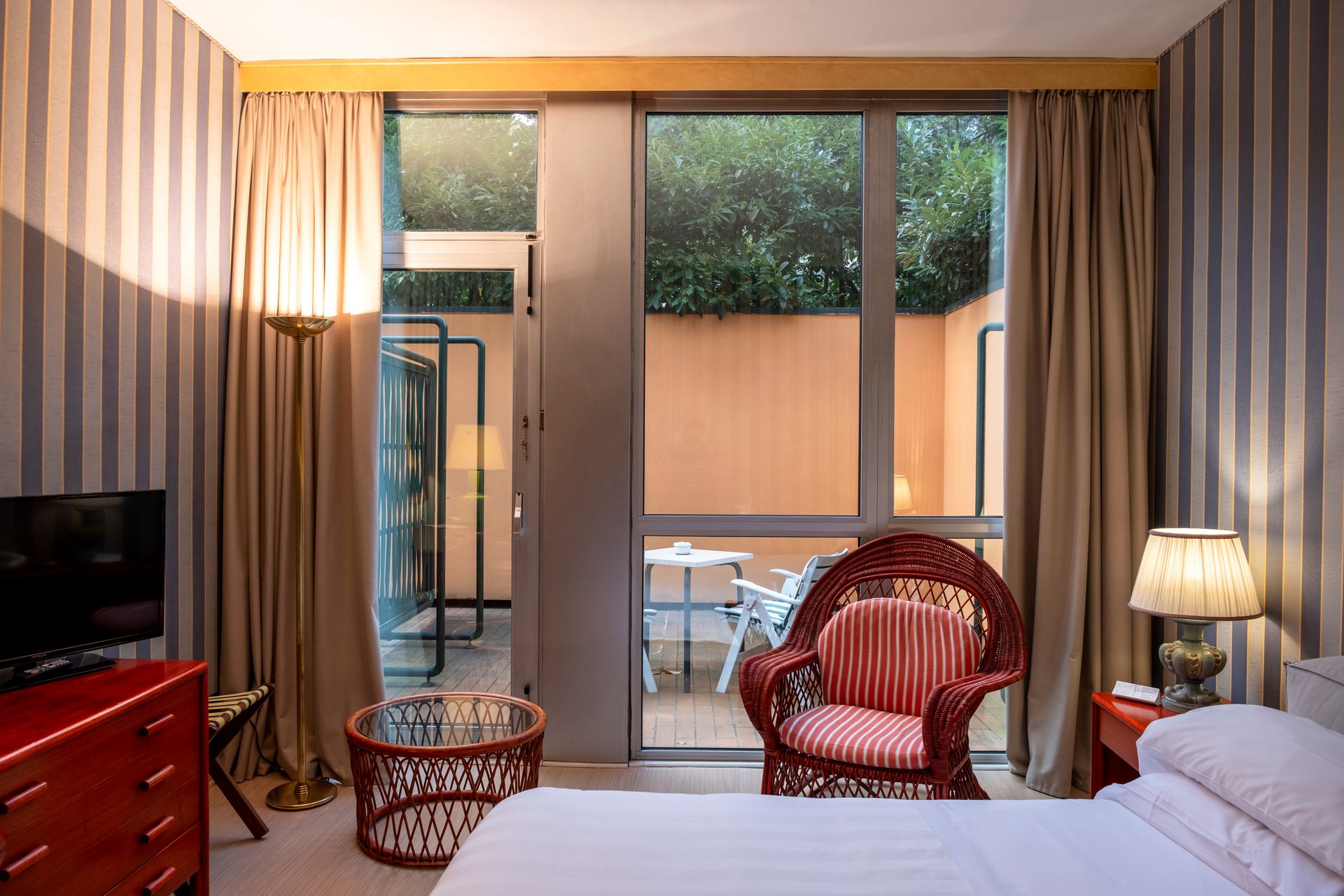 Гостиничный номер с кроватью, стулом, телевизором и полосатыми обоями.