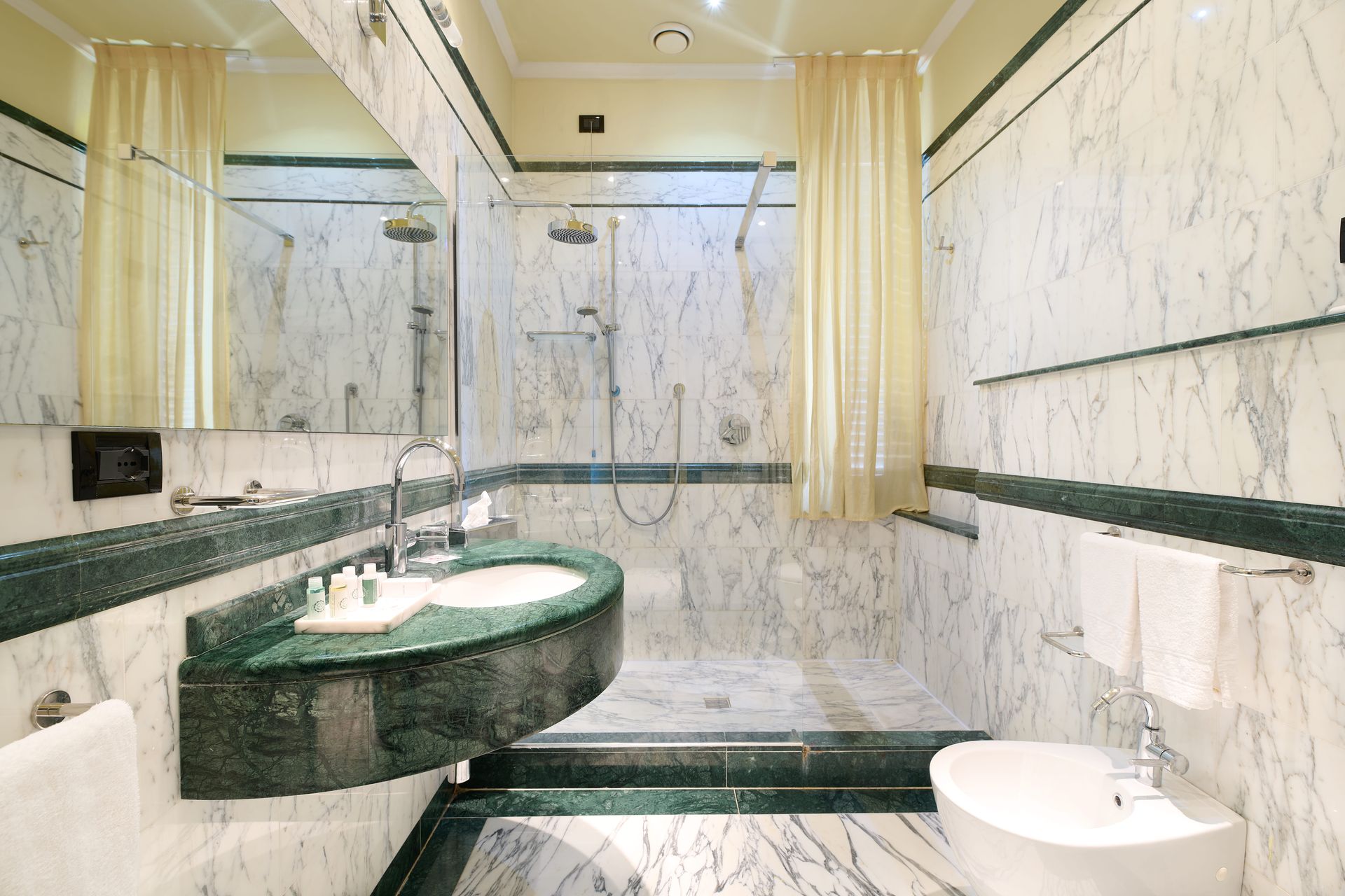 Ванная комната с мраморными стенами, раковиной, туалетом и душем.