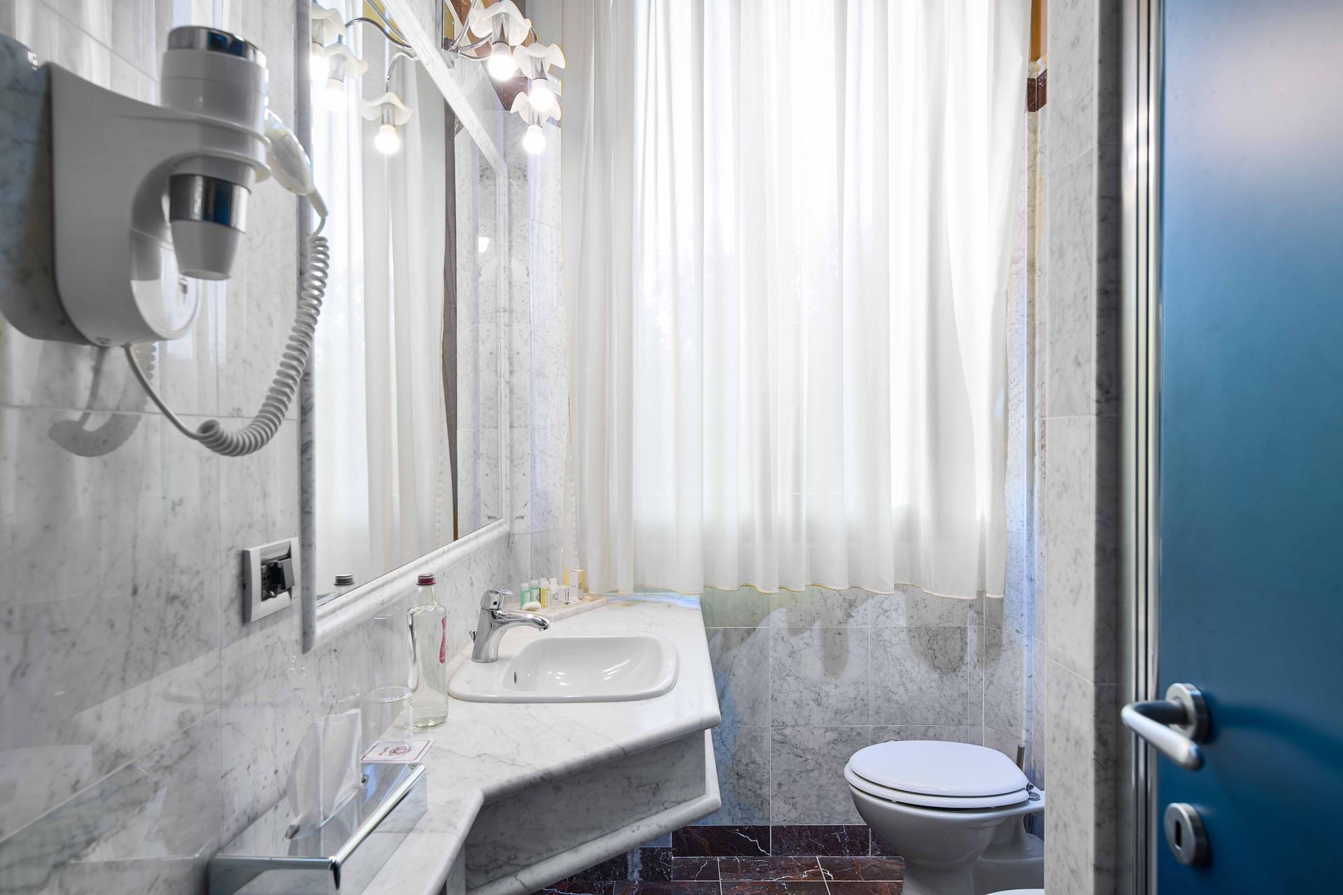 Ванная комната с туалетом, раковиной, зеркалом и феном.