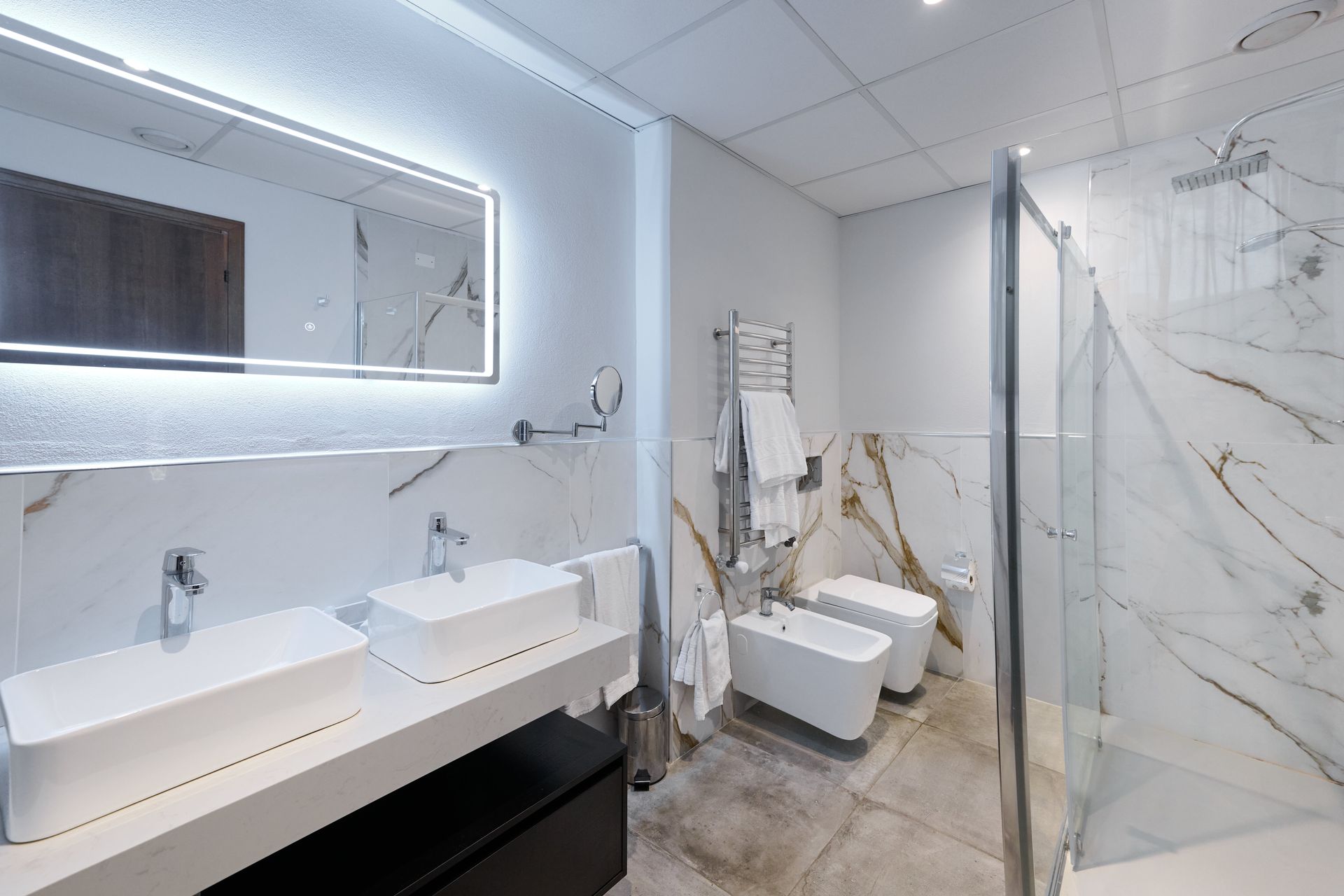 Ванная комната с двумя раковинами, двумя туалетами, душем и зеркалом.