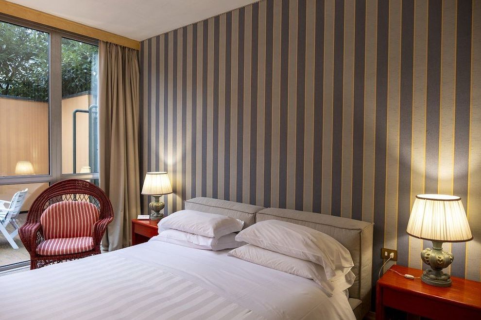 Una stanza d'albergo con un letto, una sedia, lampade e carta da parati a strisce.