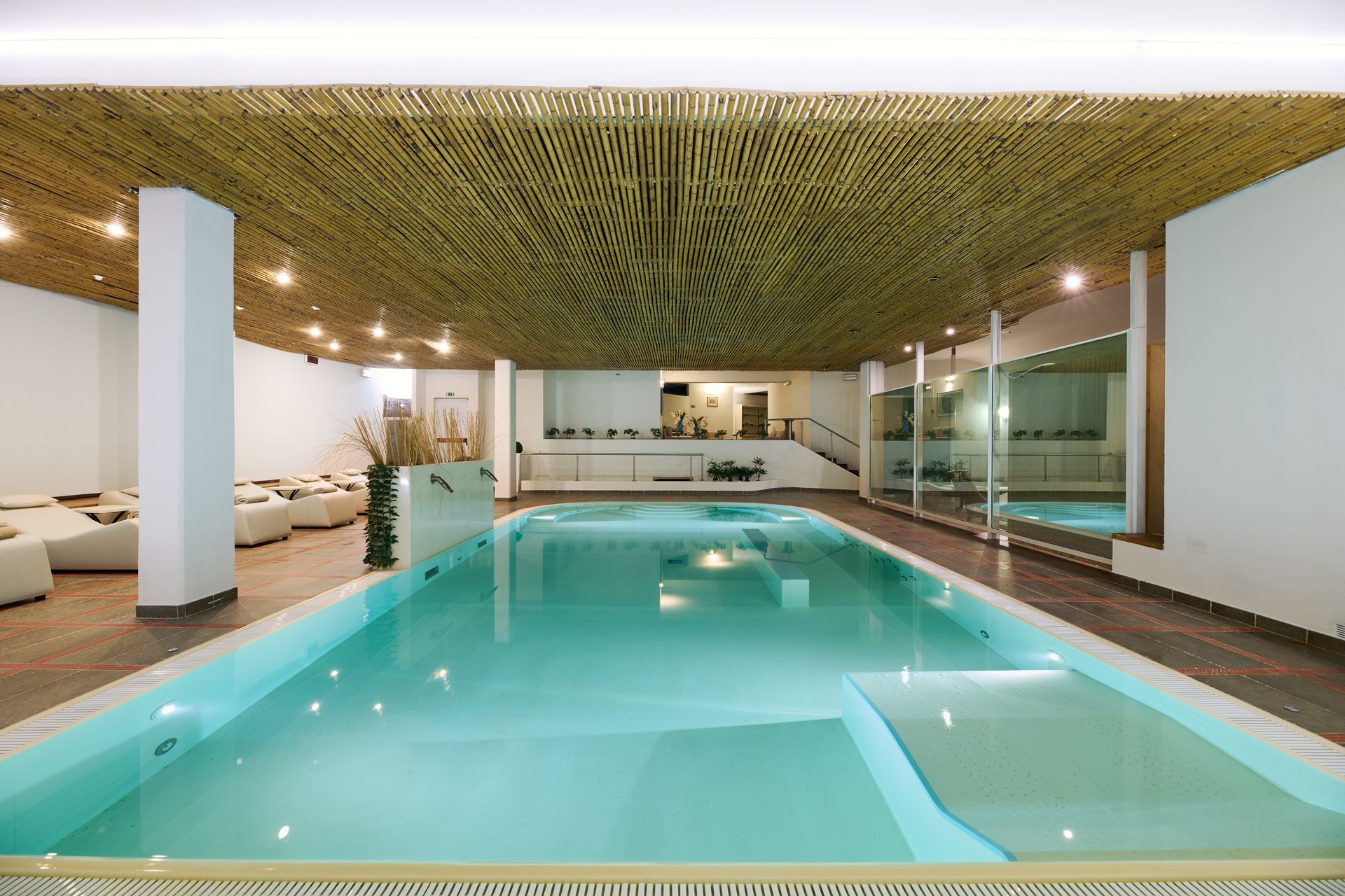 Piscina interna con acqua al magnesio, lettini relax e soffitto in legno decorato in una moderna sala spa.