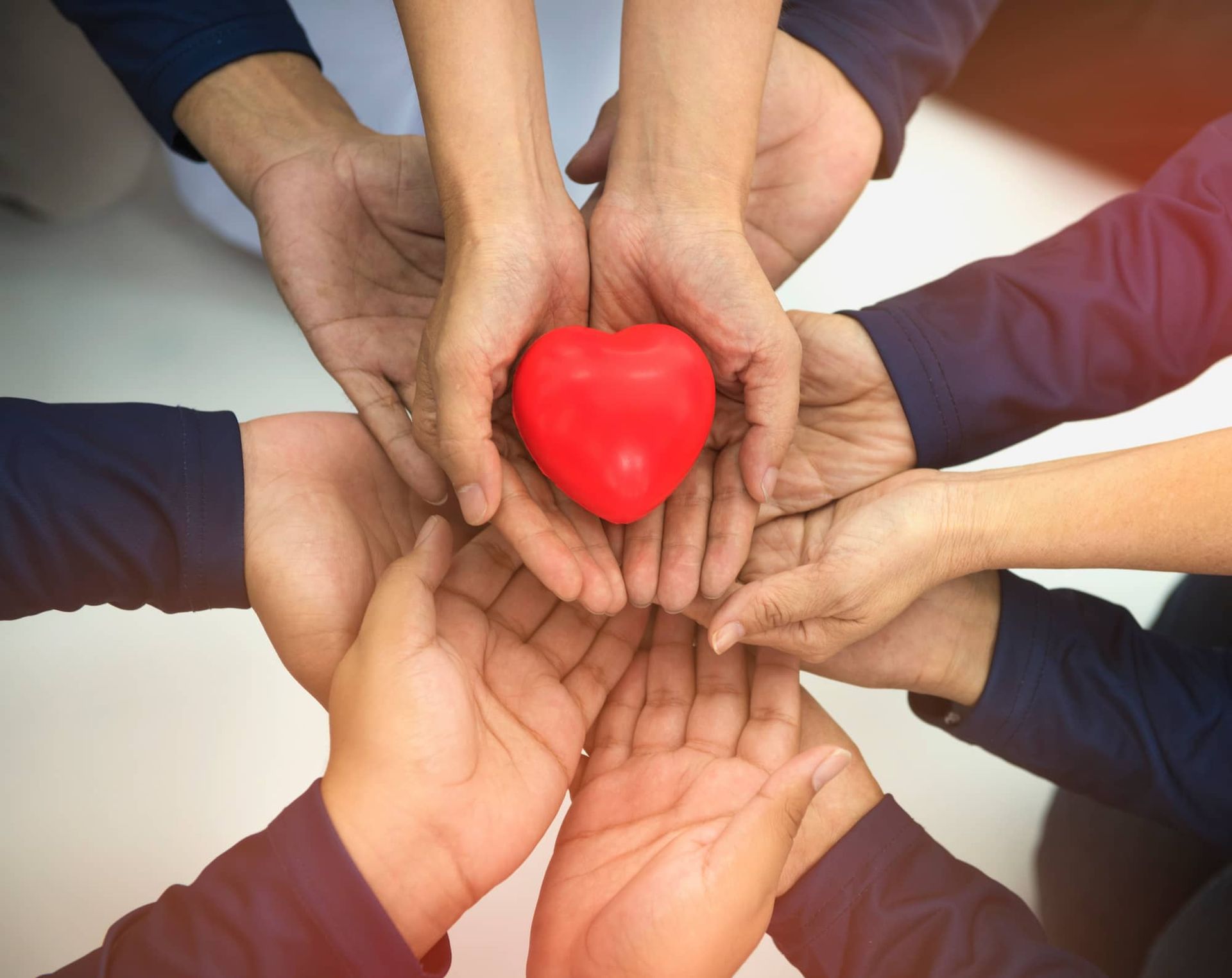 Multiple hands cupping a bright red heart, symbolizing care and teamwork