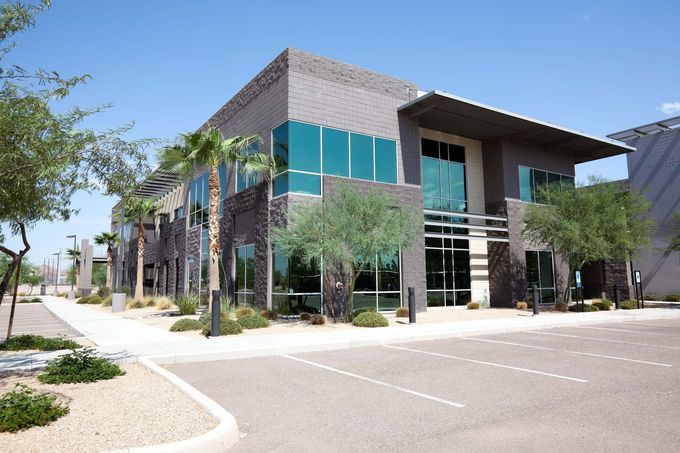 Modern office building with teal windows, brick facade, and a parking lot in front