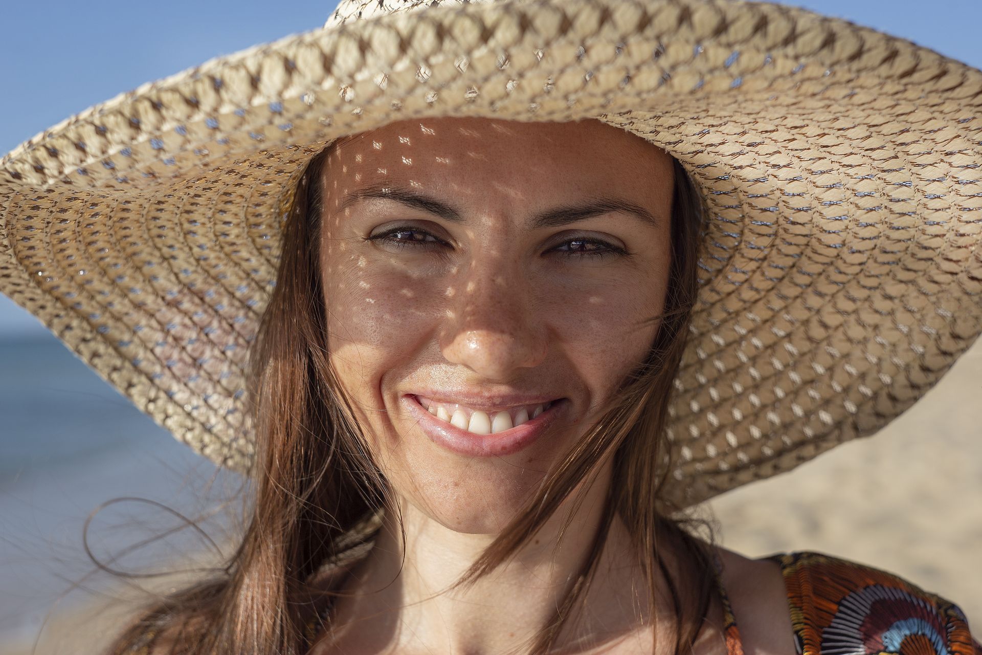 Smiling Person Wearing a Wide Straw Hat on A Sunny Beach — Clear Optometry In Bargara, QLD