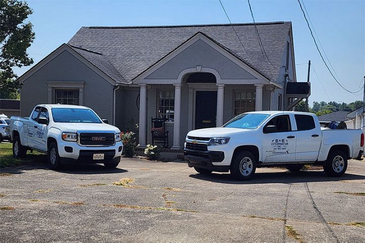 Two white pickup trucks parked in front of a small, light gray building.