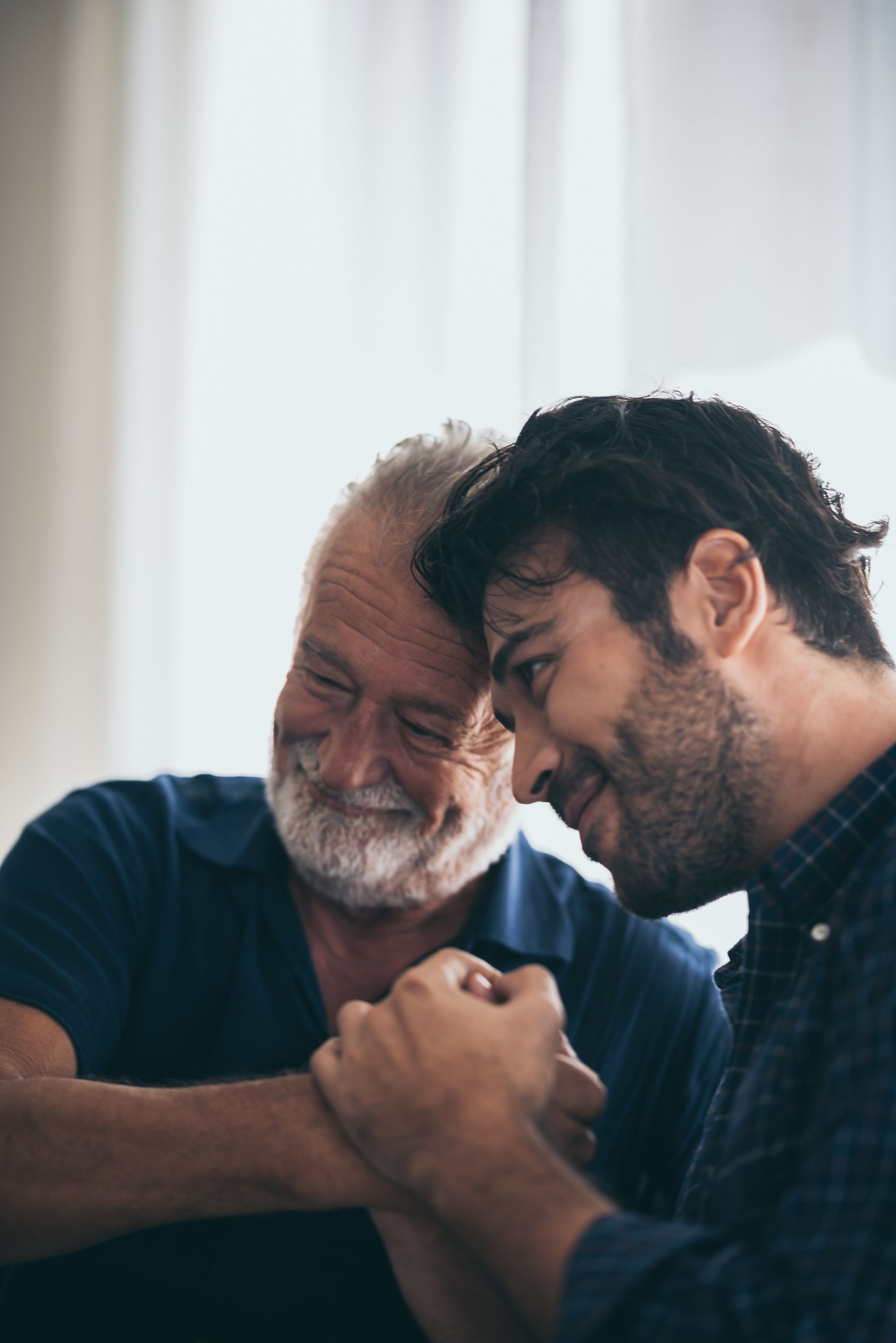 An older man with a white beard and a younger man clasp hands, both smiling.