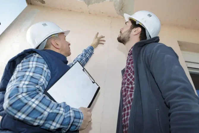 Two inspectors examine wall cracks.