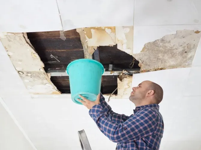 Man catching water from leaking ceiling in bucket.