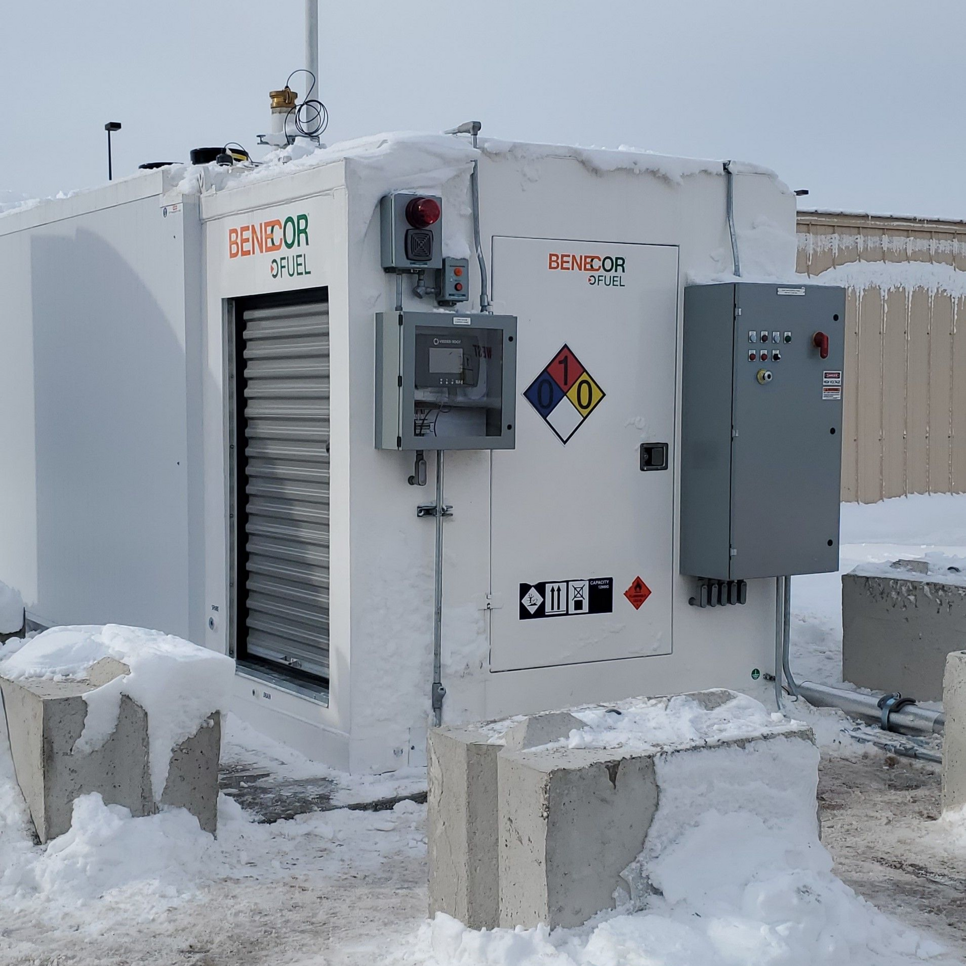 White fuel storage unit with snow, hazard labels, and control panel.