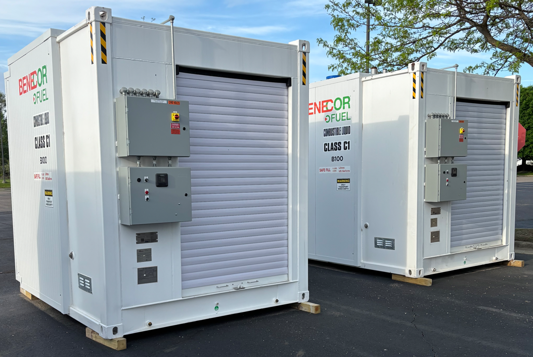 Two white industrial containers with roll-up doors and electrical boxes, sitting outdoors on a parking lot.