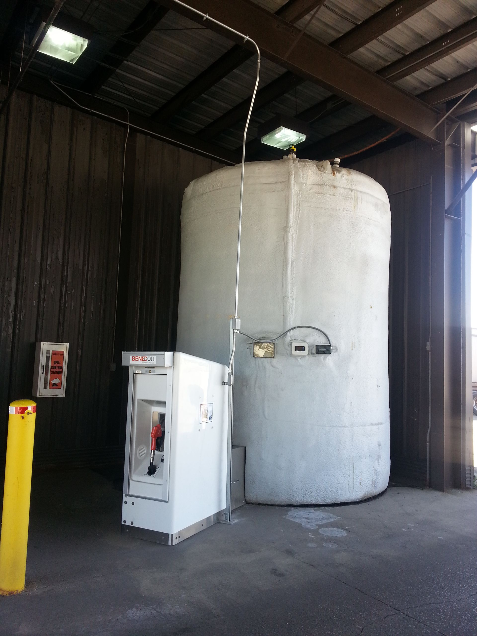 White liquid oxygen tank and dispensing unit under a shelter. Fire alarm and yellow bollard post are visible.