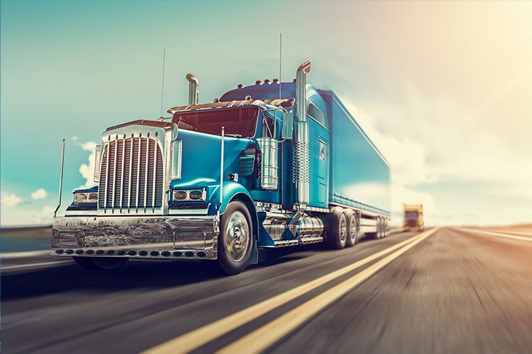 Blue semi-truck on highway with a trailer. Bright sunlight, a clear sky.
