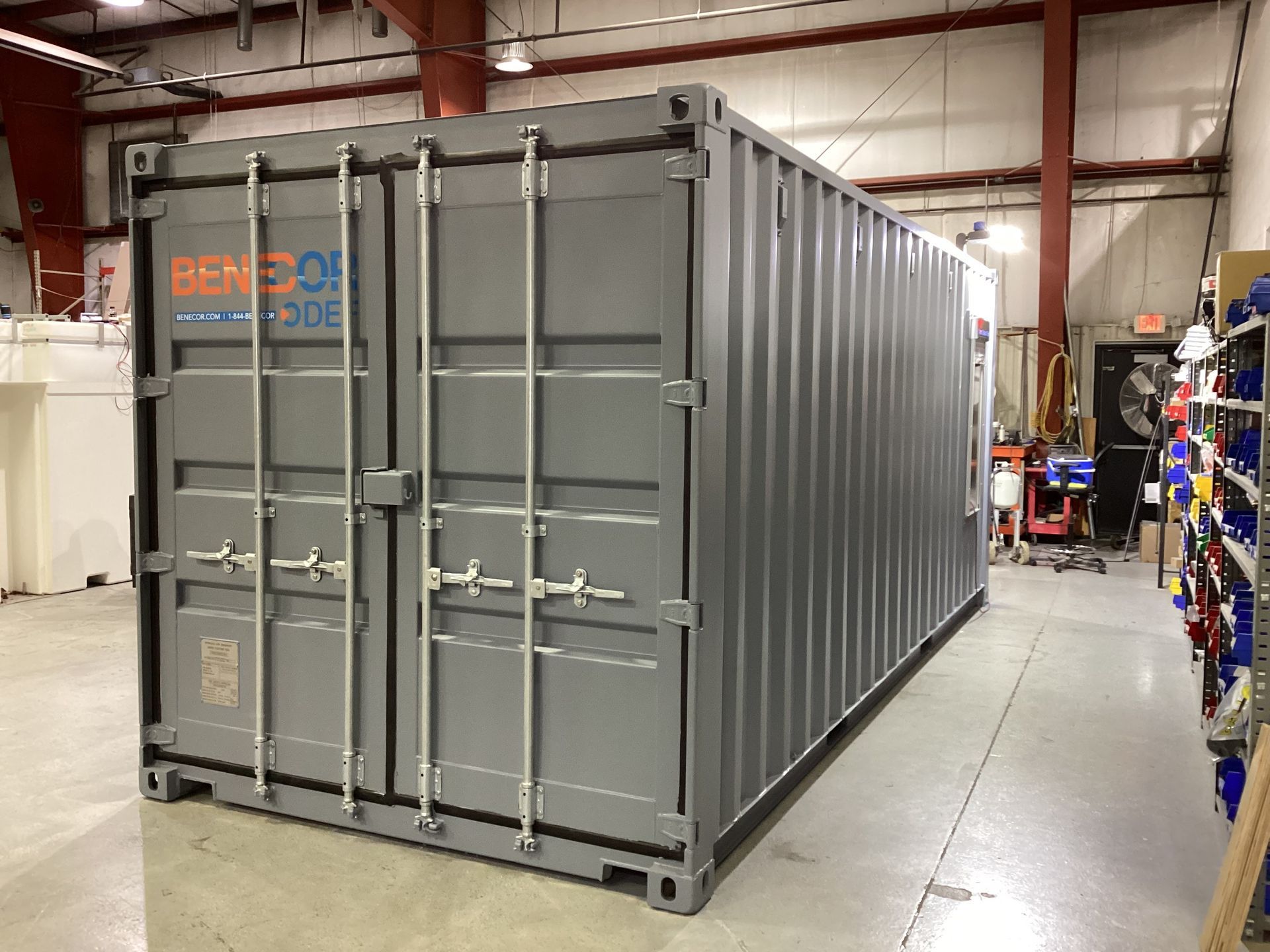 Gray shipping container inside a warehouse, with logos on the front doors.