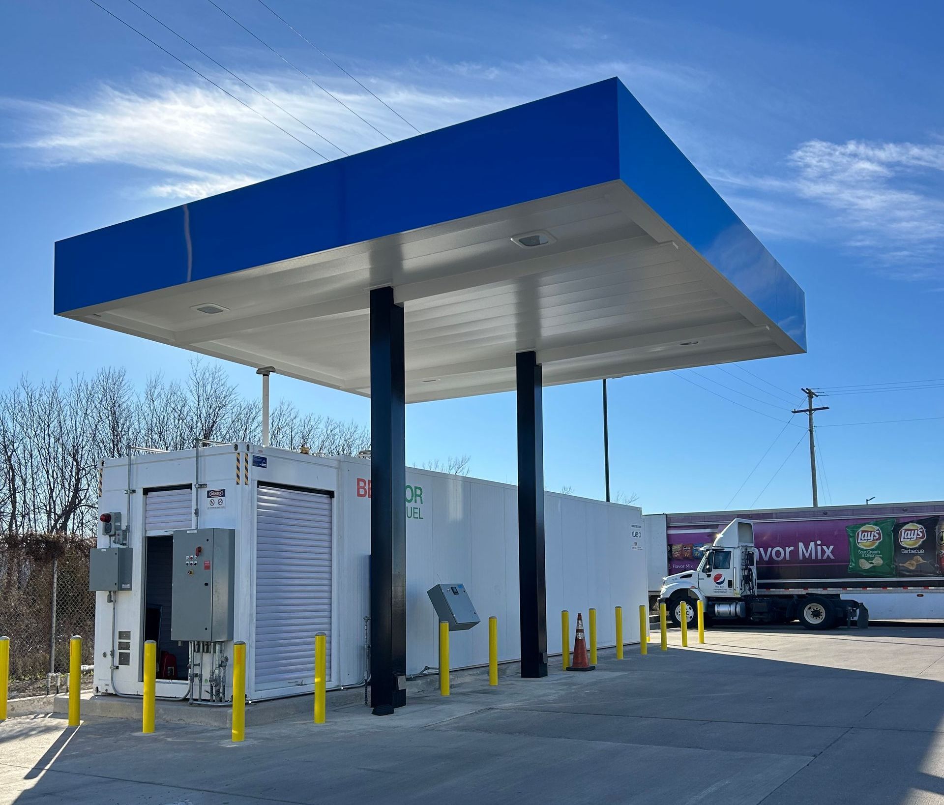 Gas station canopy with a blue top, black columns, and a white building, truck parked nearby.