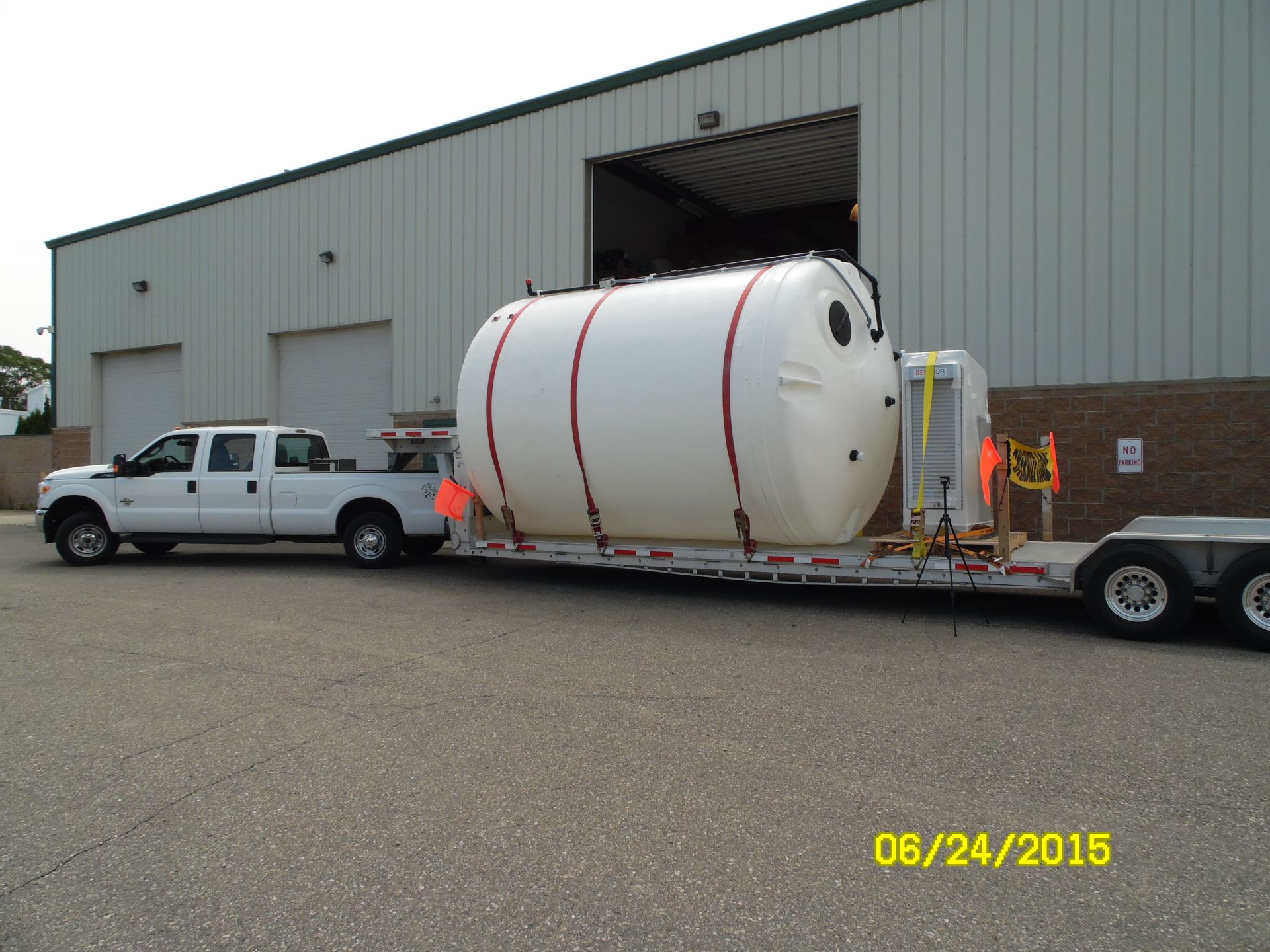 White truck towing a large white tank on a trailer near a building.