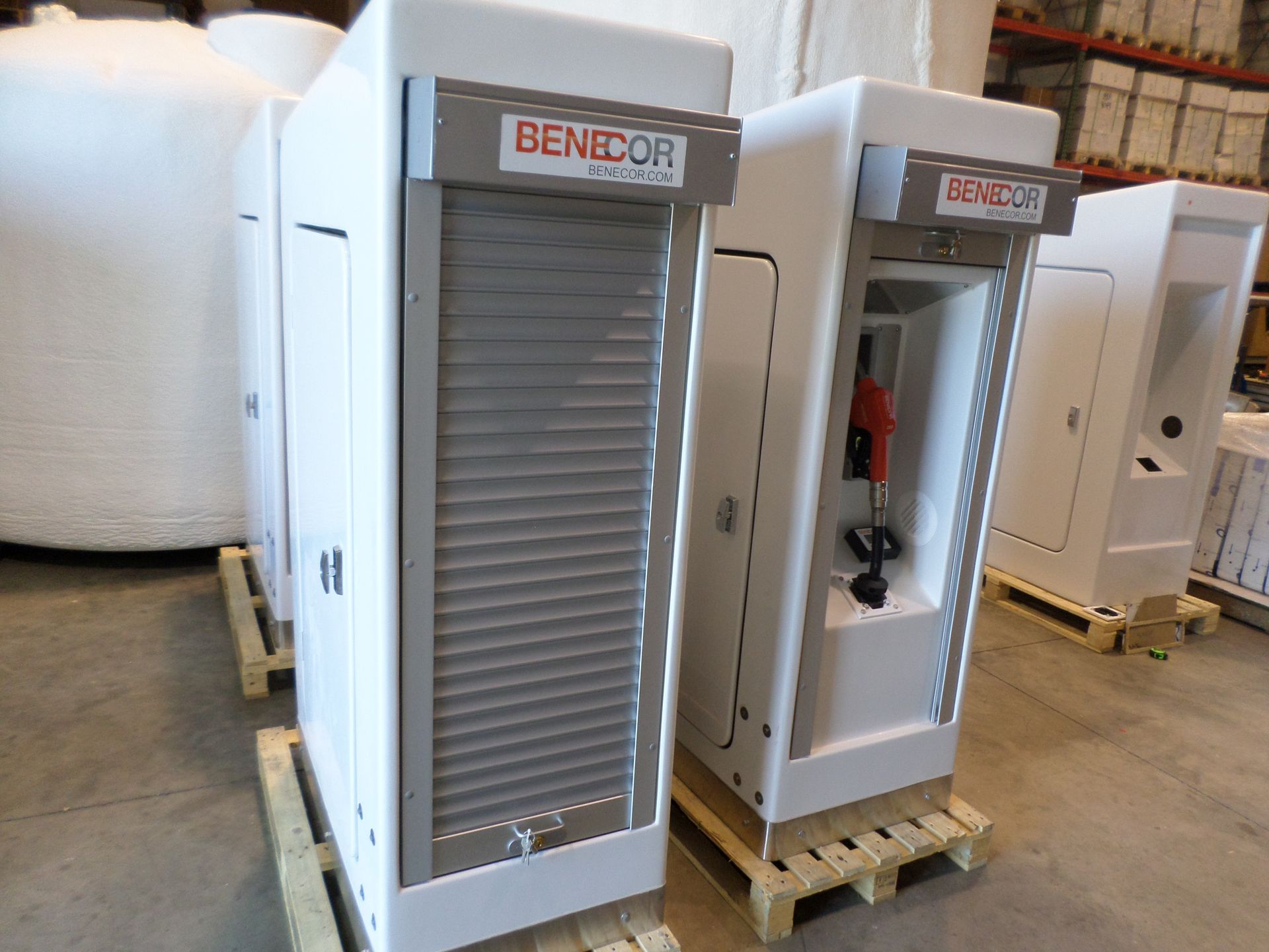 White BeneCor industrial cabinets on pallets. One with a roll-up door, the other with red nozzle, inside warehouse.