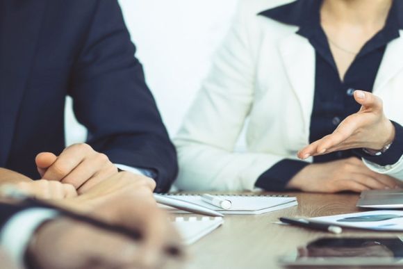 Riunione di lavoro con persone in giacca e cravatta che discutono di documenti attorno a un tavolo.