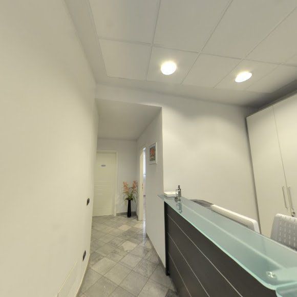 Luminosa e moderna area reception con pareti bianche, scrivania in vetro e faretti a incasso a soffitto.