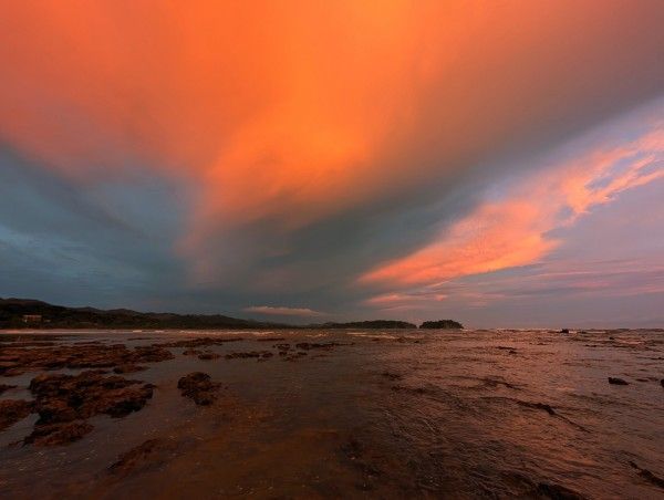 Sunset over a rocky beach with vibrant orange and gray clouds.