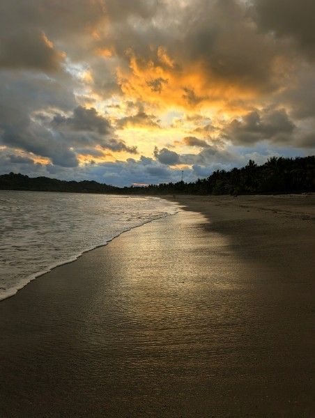 Beach at sunset, waves rolling onto shore under a cloudy, golden sky.
