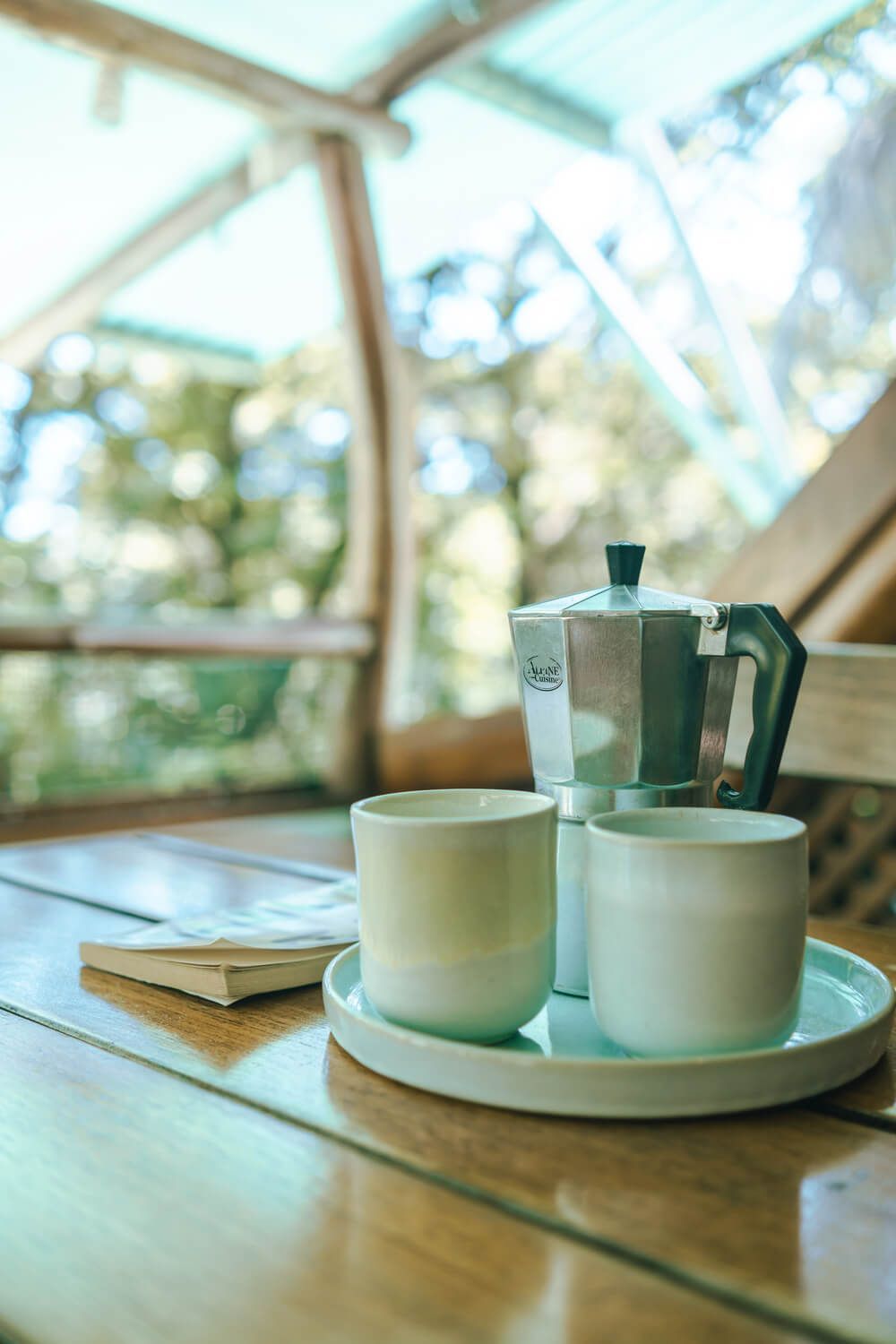 Coffee pot and cups on a tray set on a wooden table, outside with natural light.