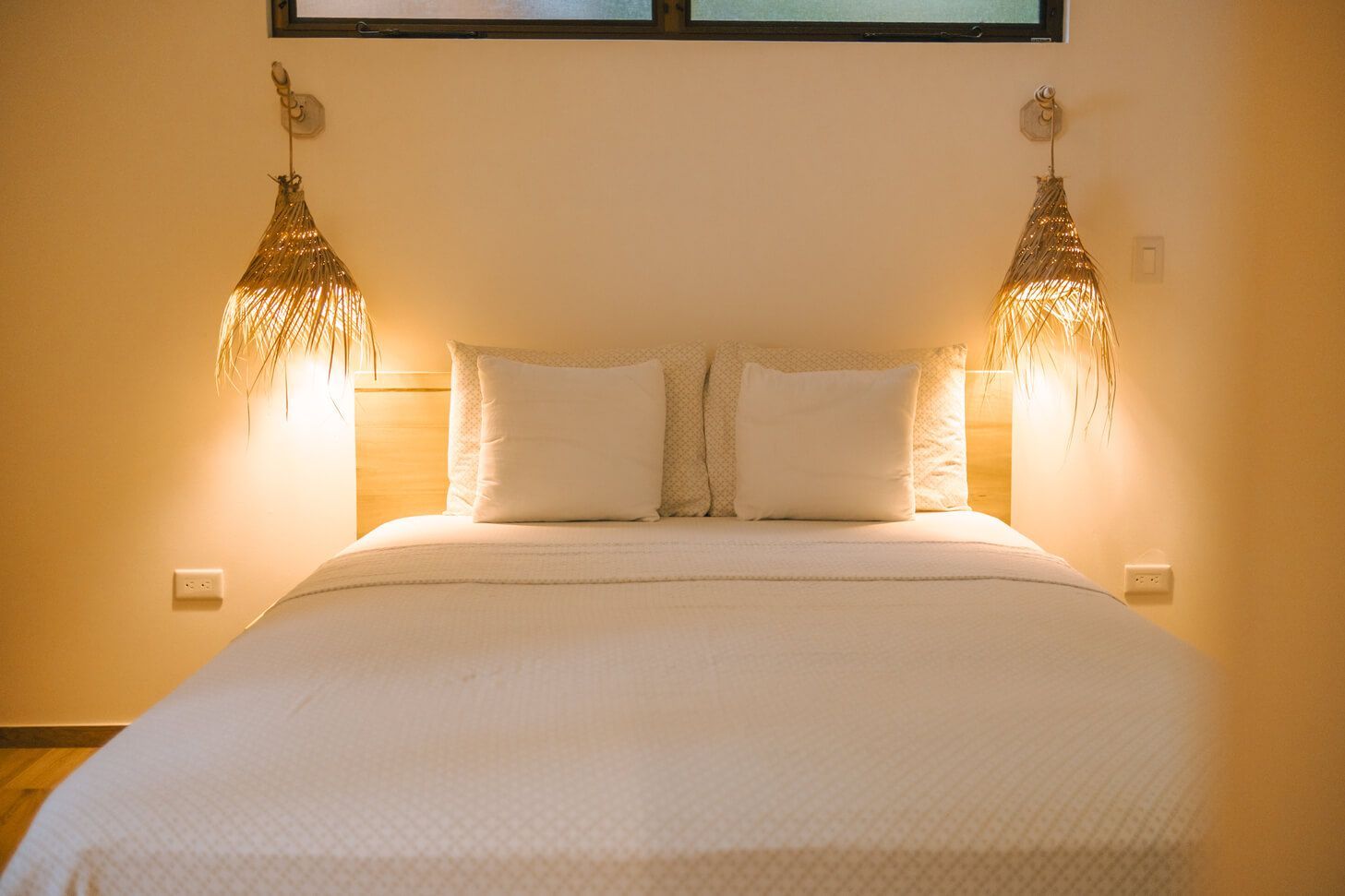 Bedroom with bed, two white pillows, woven lamps hanging above.