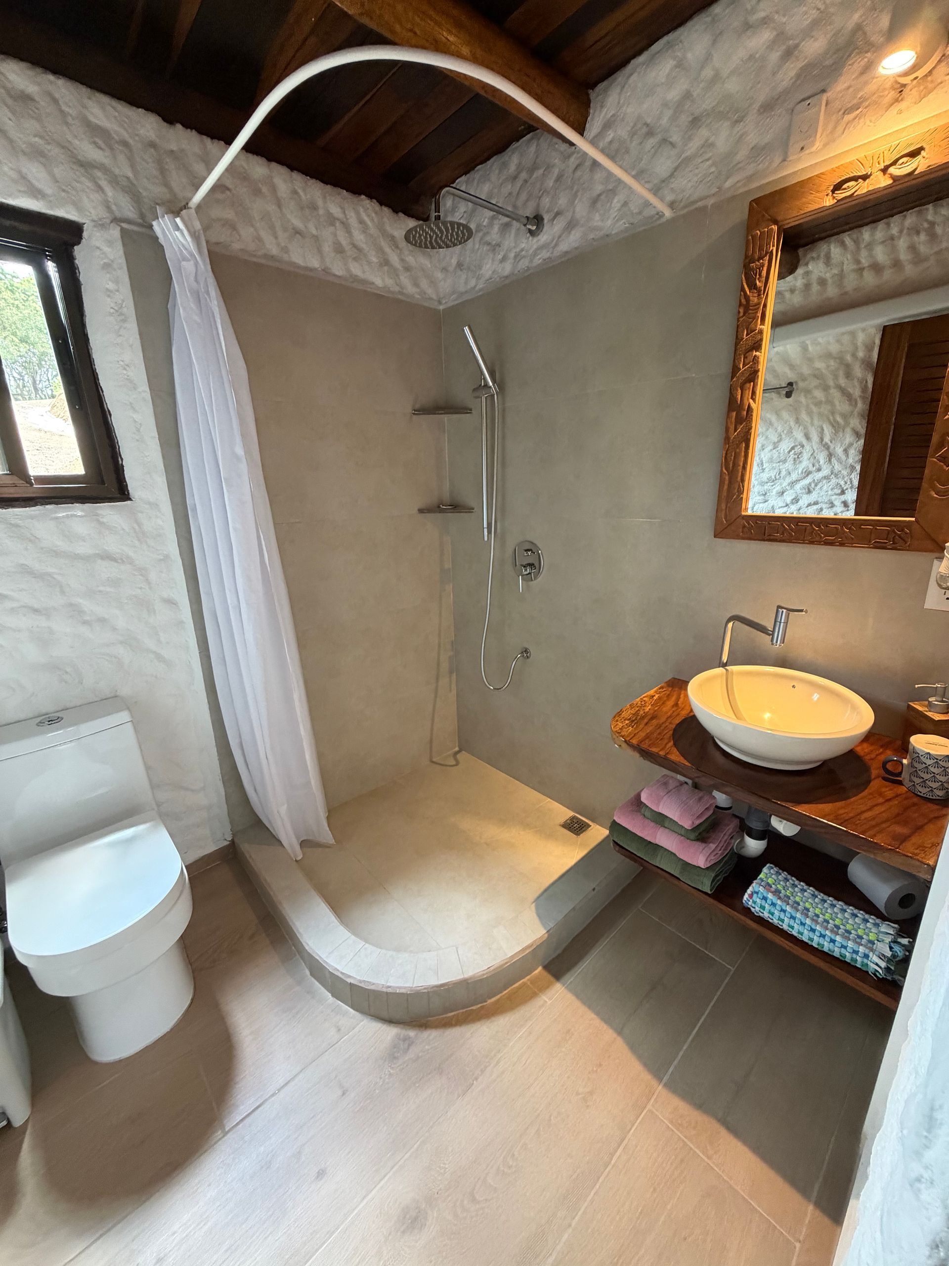 Small bathroom with shower, toilet, sink, and wood-framed mirror under a sloped ceiling.