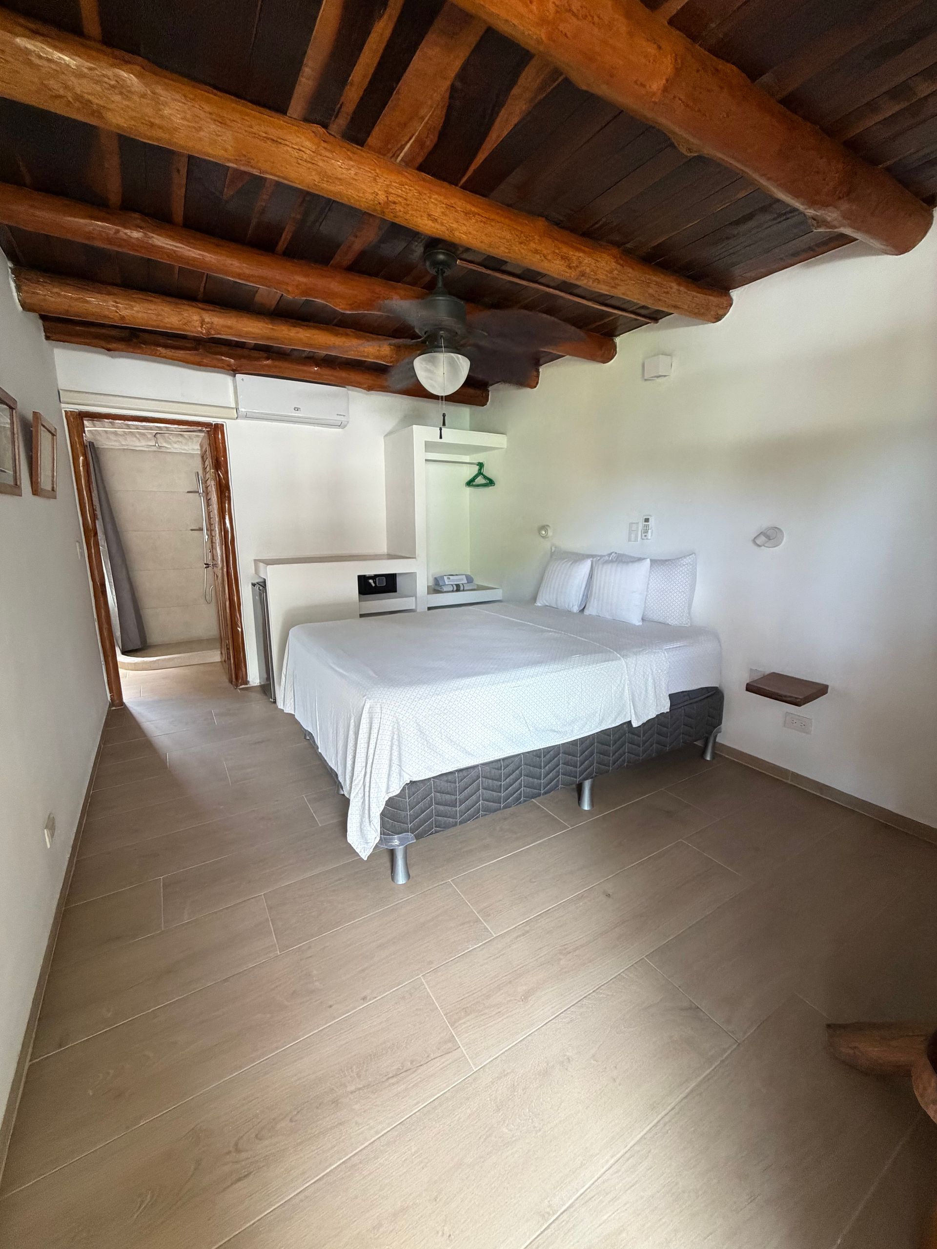 Rustic bedroom with exposed wooden beams, a bed, and a doorway to a bright hall.