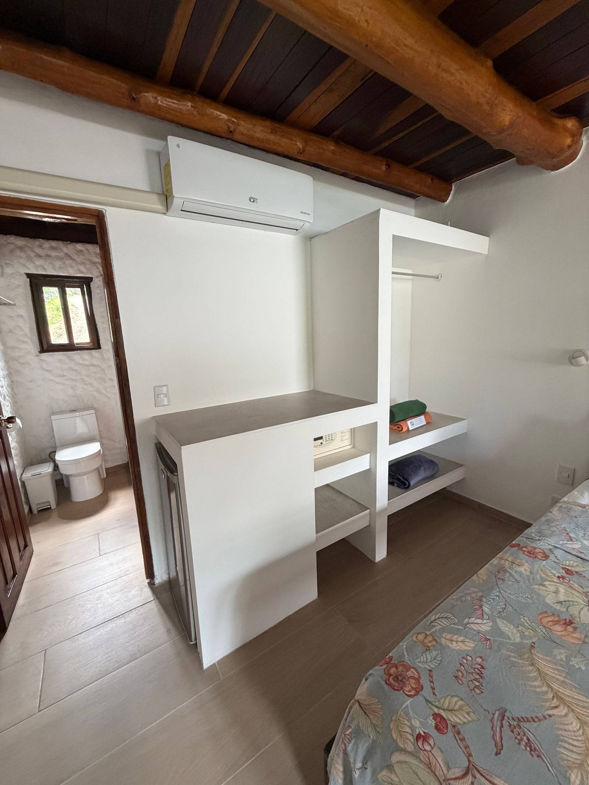 Small bedroom with a white loft bed, tiled floor, exposed wood beams, and an open doorway.