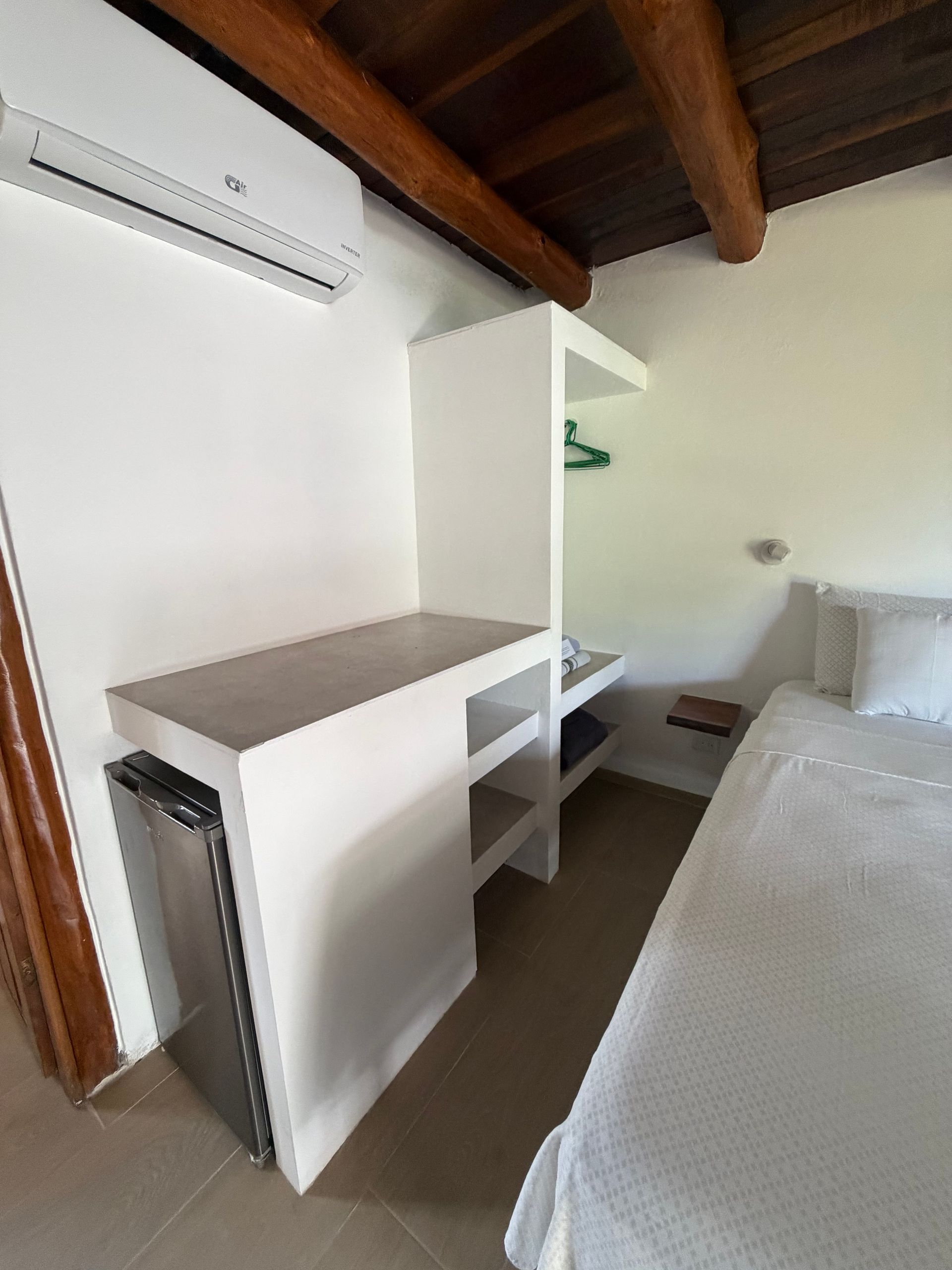 Small room with white walls, a loft bed, built-in shelves, and an air conditioner under wooden ceiling beams