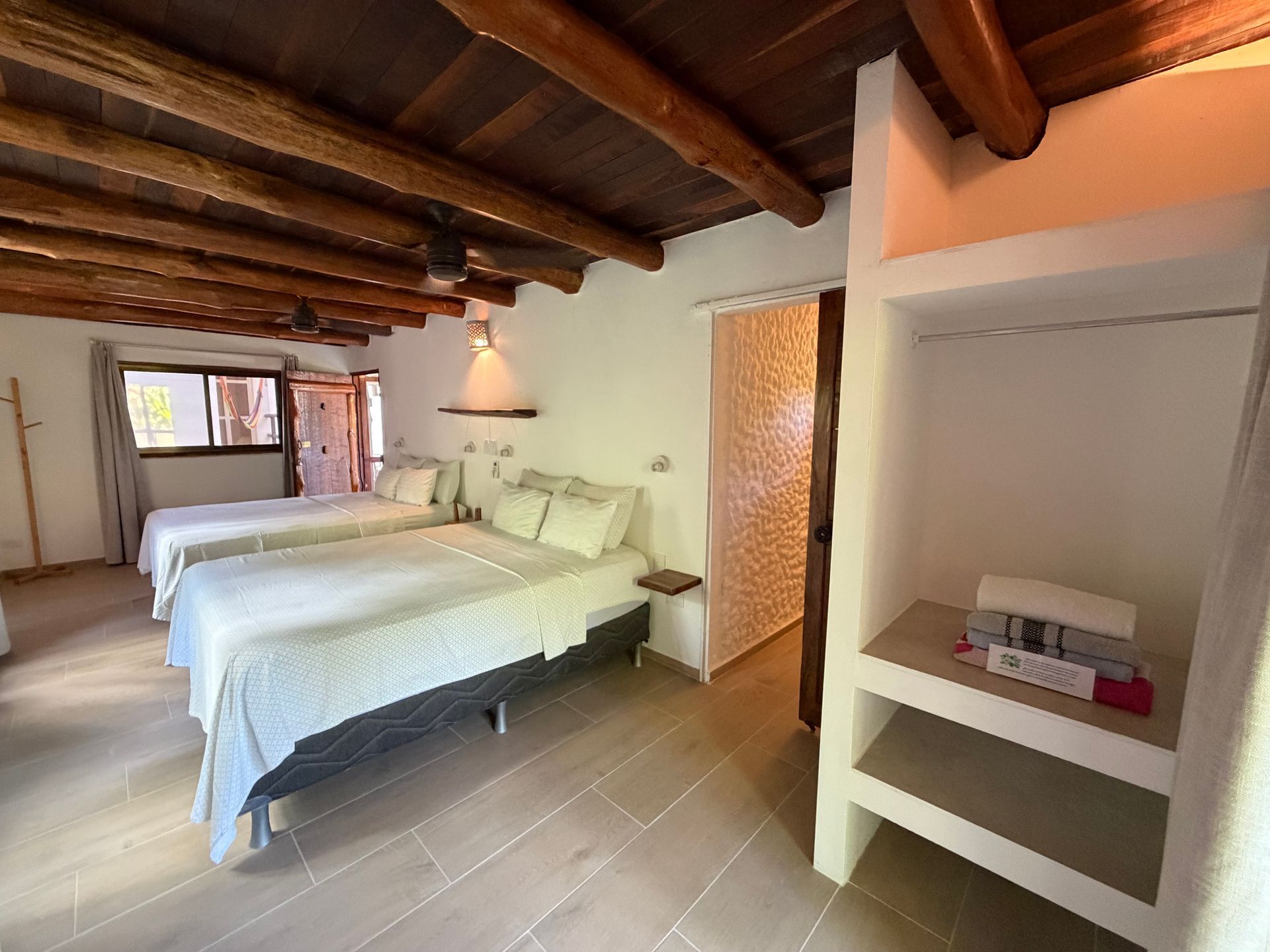 Cozy bedroom with two beds, exposed wooden beams, and a window with warm light