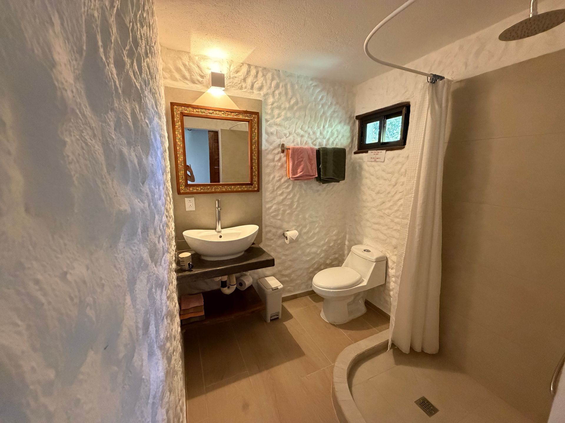 Small rustic bathroom with vessel sink, toilet, shower curtain, and wall mirror in warm light
